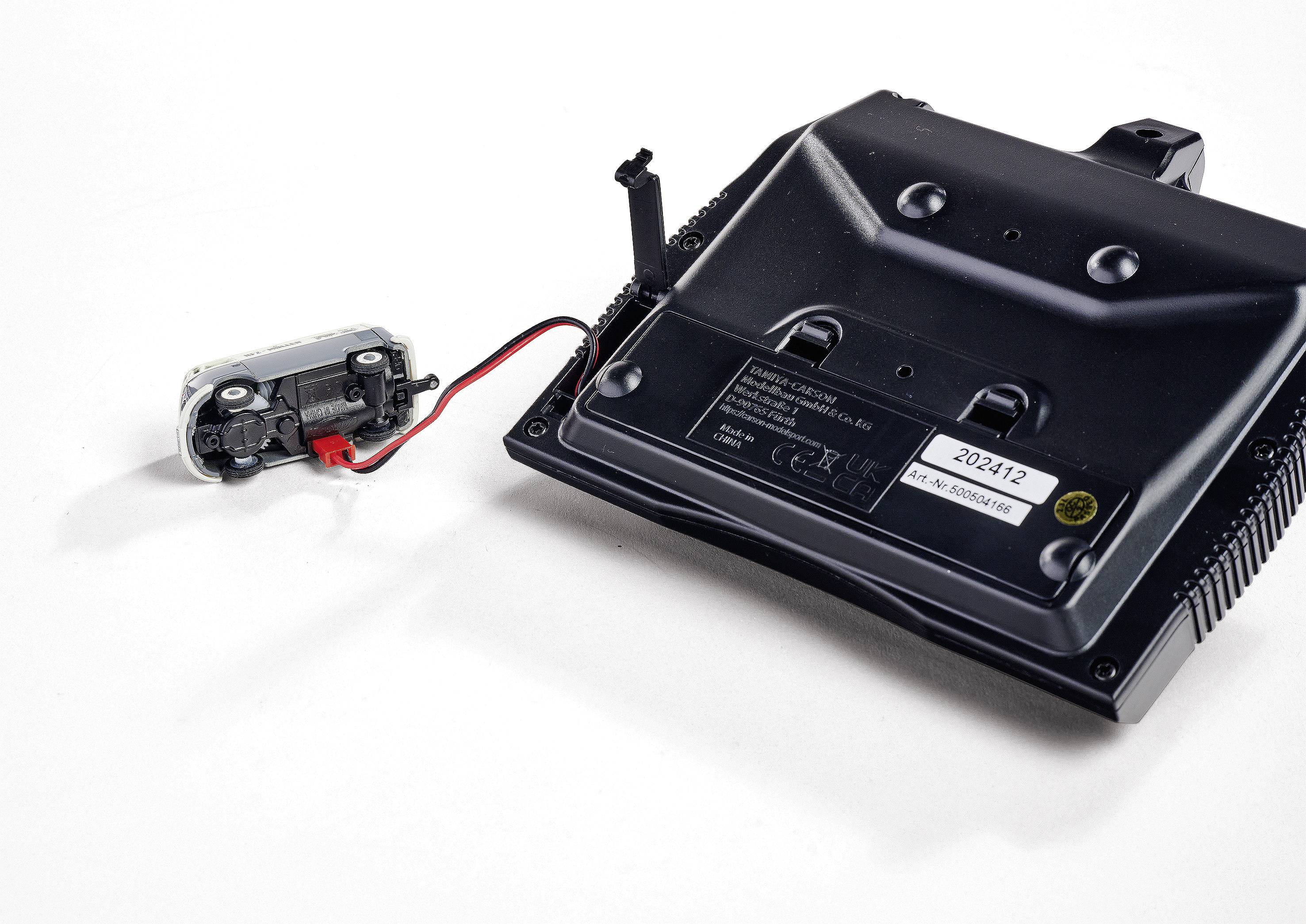 Czarne urządzenie techniczne z różnymi złączami i zamocowanym mniejszym modułem z czerwonym i czarnym przewodem.