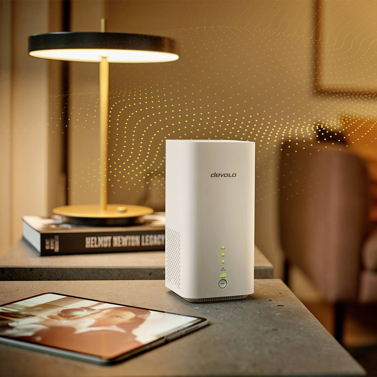 Router Wi-Fi leżący na stole obok tabletu i lampy. Tło lekko rozmyte, fokus na routerze z zielonymi świecącymi diodami LED.