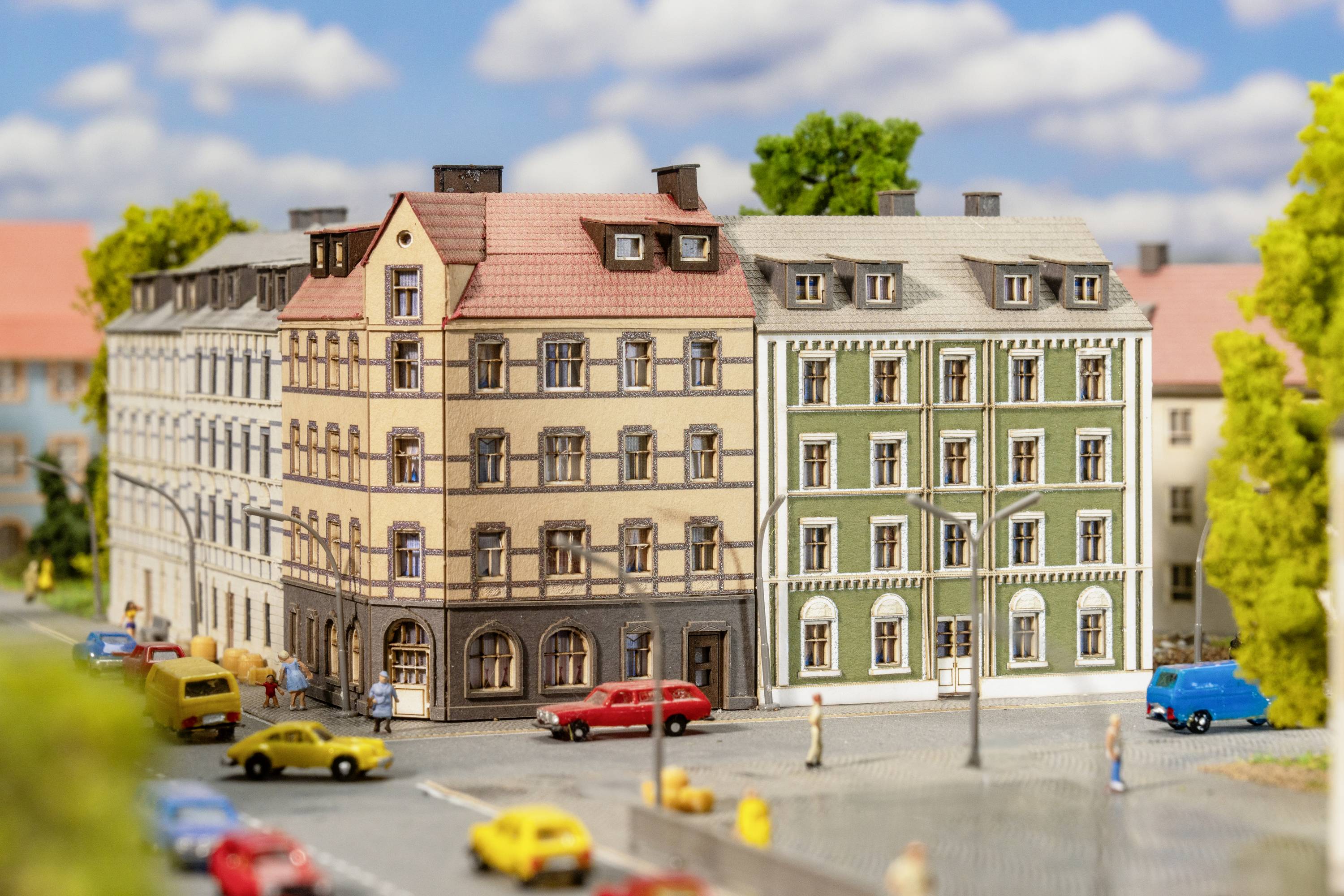 Wielopiętrowe kamienice staromiejskie z czerwonymi i zielonymi elewacjami, samochody i piesi na zatłoczonej ulicy pod błękitnym niebem.