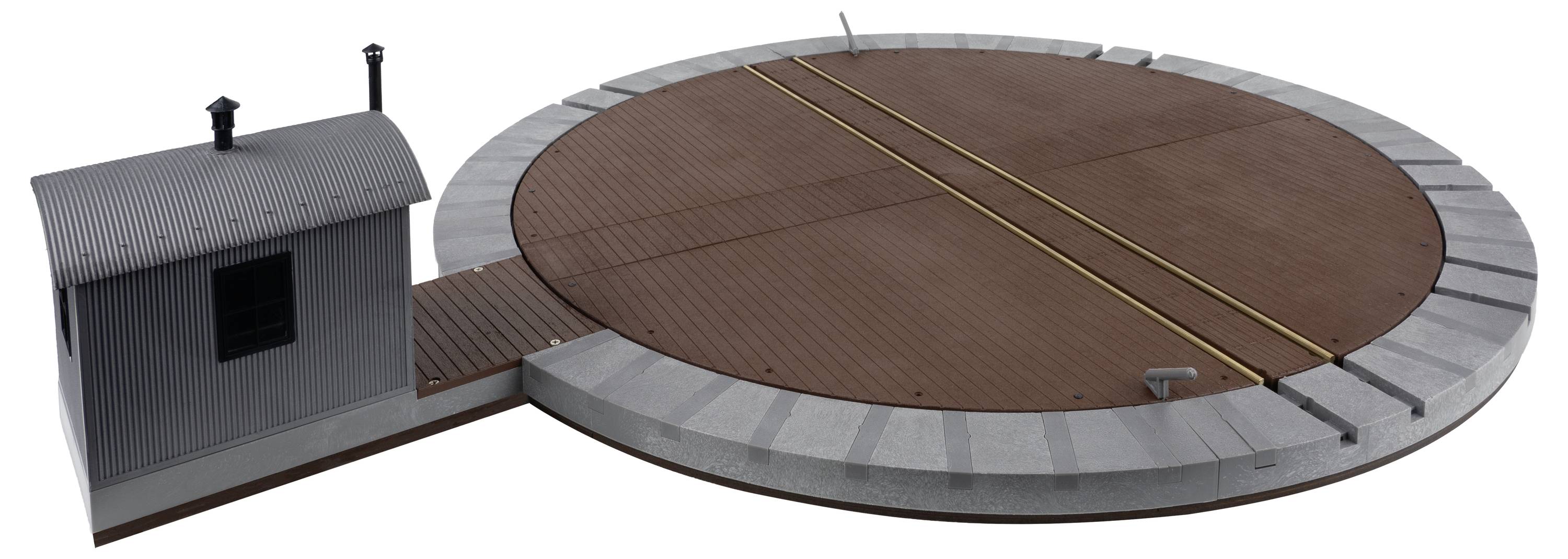 Obrotnica kolejowa dla modeli pociągów z małym, przylegającym budynkiem z blachy falistej po lewej stronie.