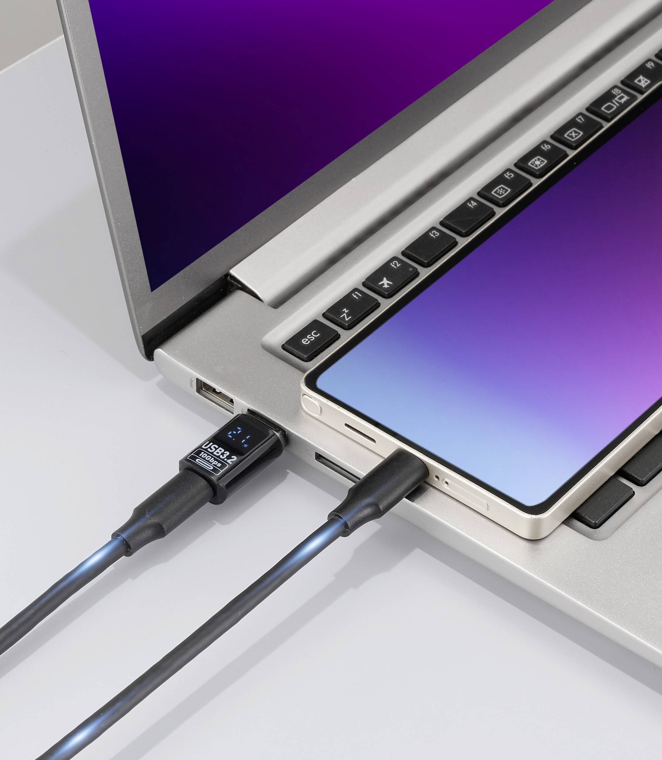 Smartfon jest podłączony do laptopa za pomocą kabla USB, z dodatkowym złączem USB wpiętym do laptopa, co wskazuje na transfer danych.