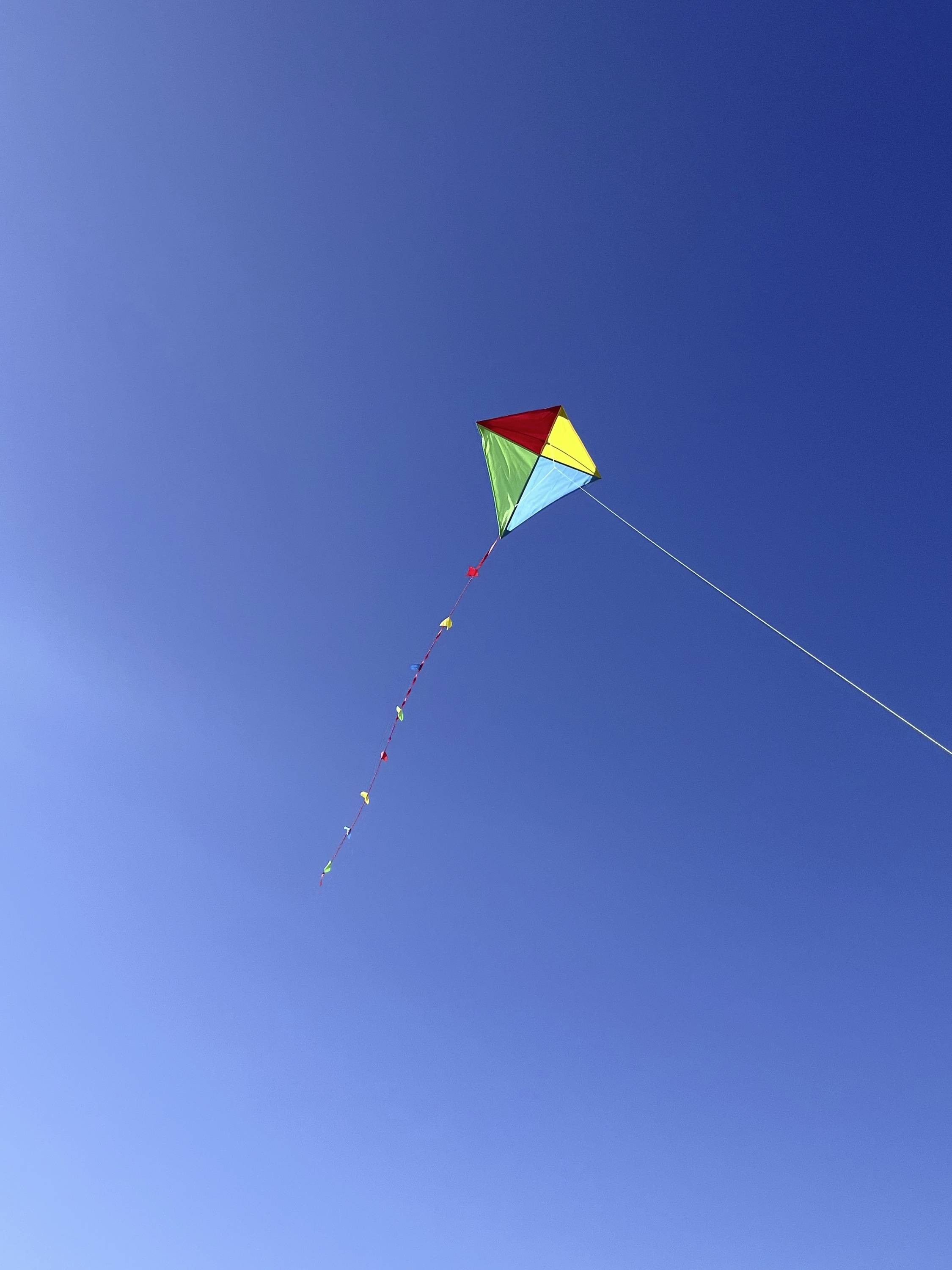 Kolorowy smok unosi się na czystym, błękitnym niebie, ciągnąc za sobą długi, wielobarwny ogon.