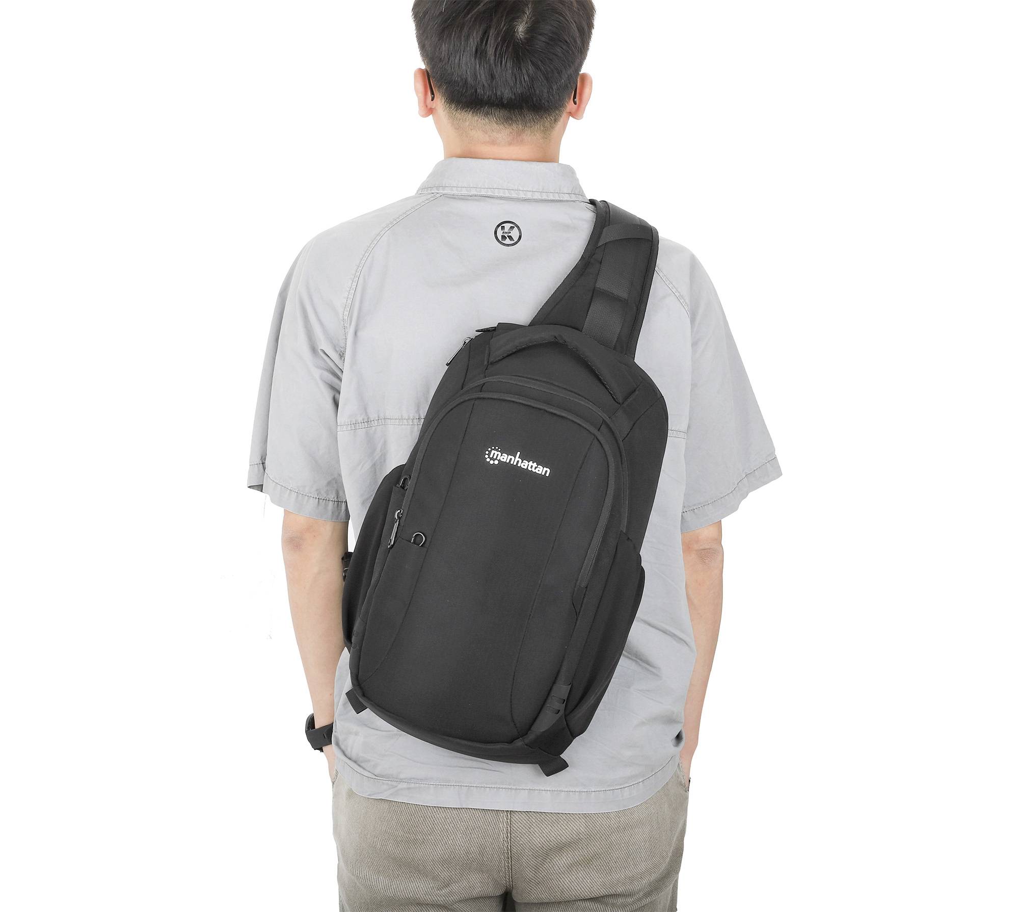 Mężczyzna widziany od tyłu, ubrany w szarą koszulę, nosi czarny plecak przewieszony przez lewą ramię.