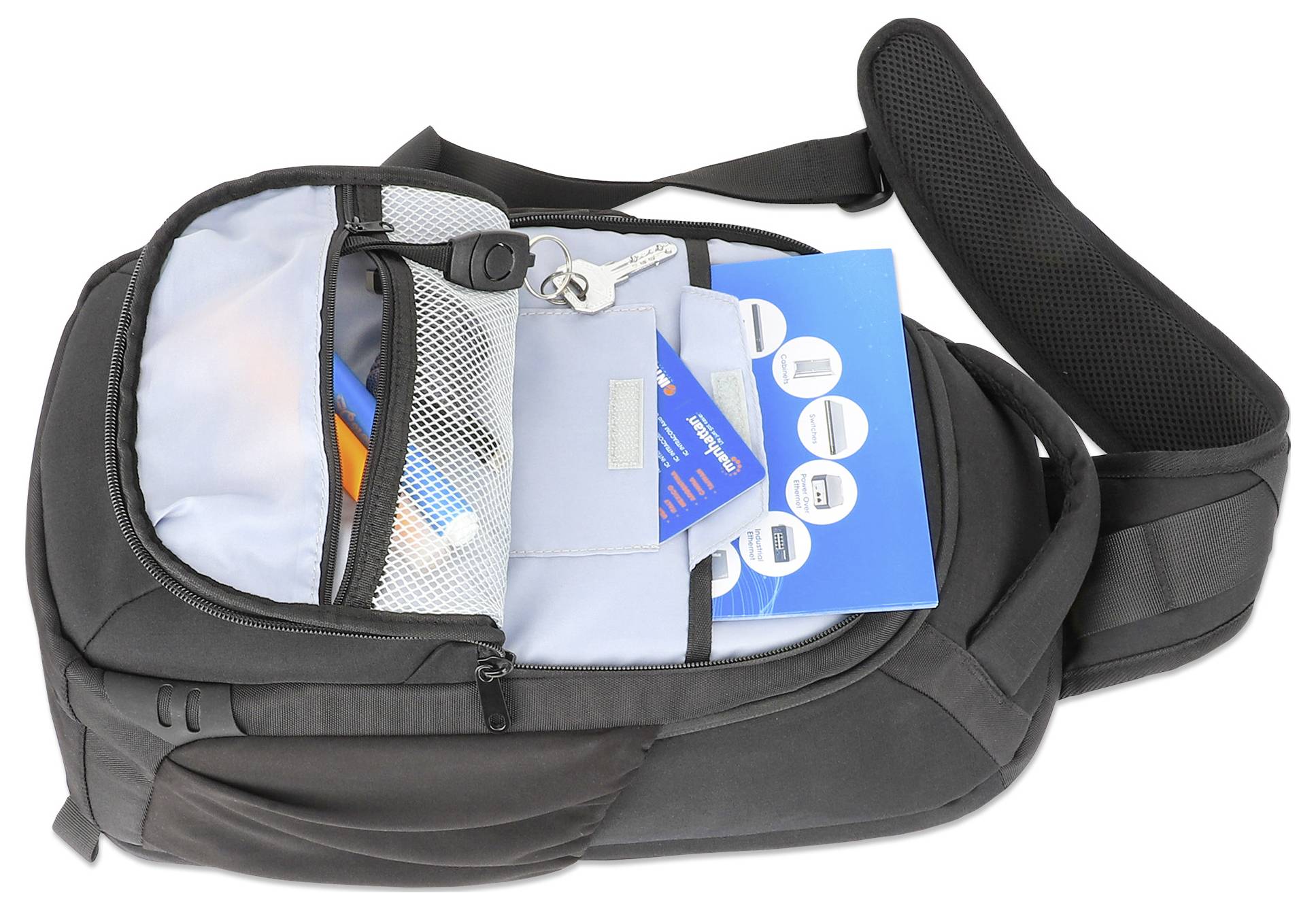 Otwarty czarny plecak ukazuje wewnętrzne kieszenie z widocznymi kluczami, niebieskimi dokumentami i pomarańczowym przedmiotem.