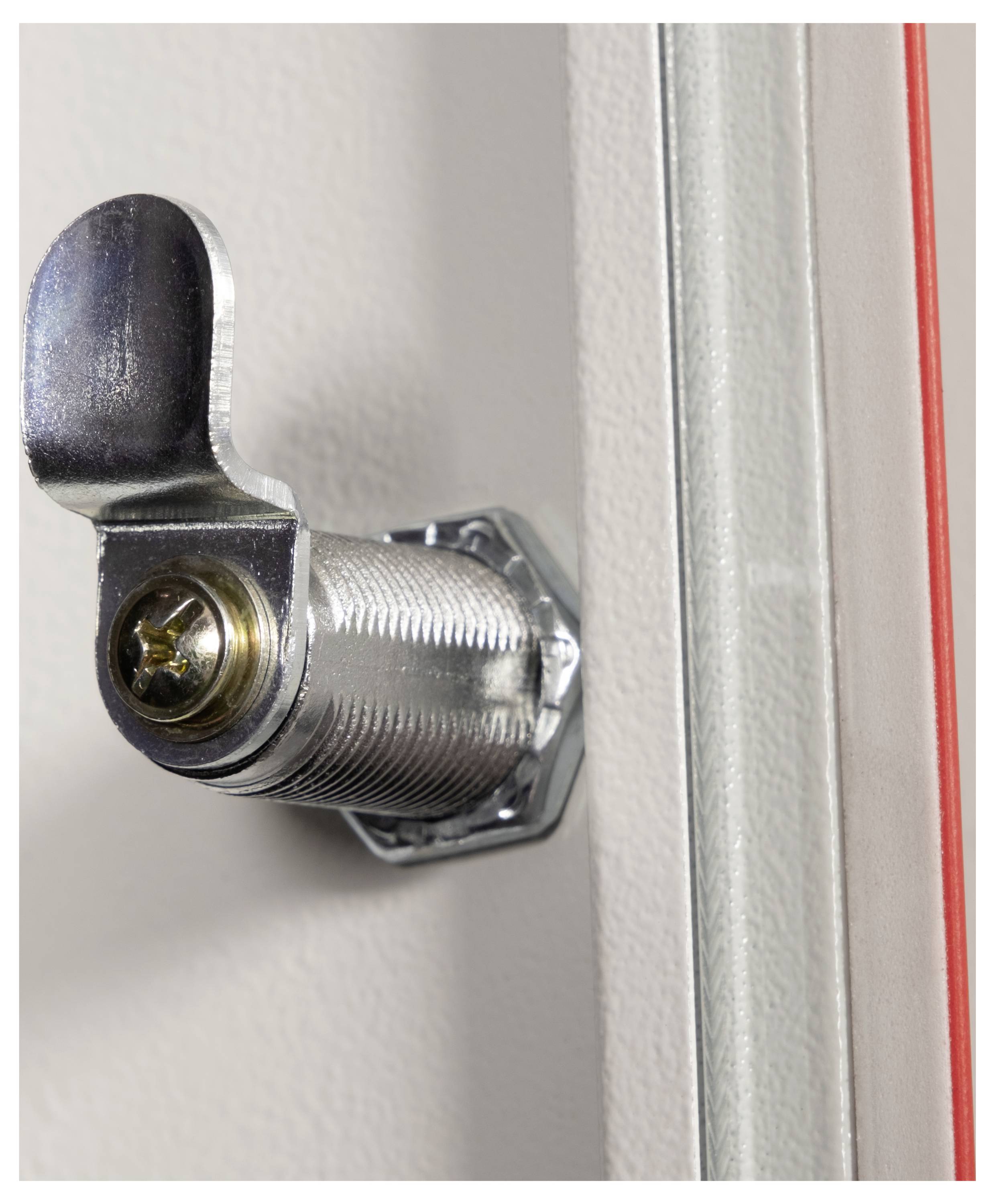 Metalowy zamek krzywkowy na szafce lub drzwiach, lekko przekręcony, z widoczną sześciokątną nakrętką i metalicznym wykończeniem.