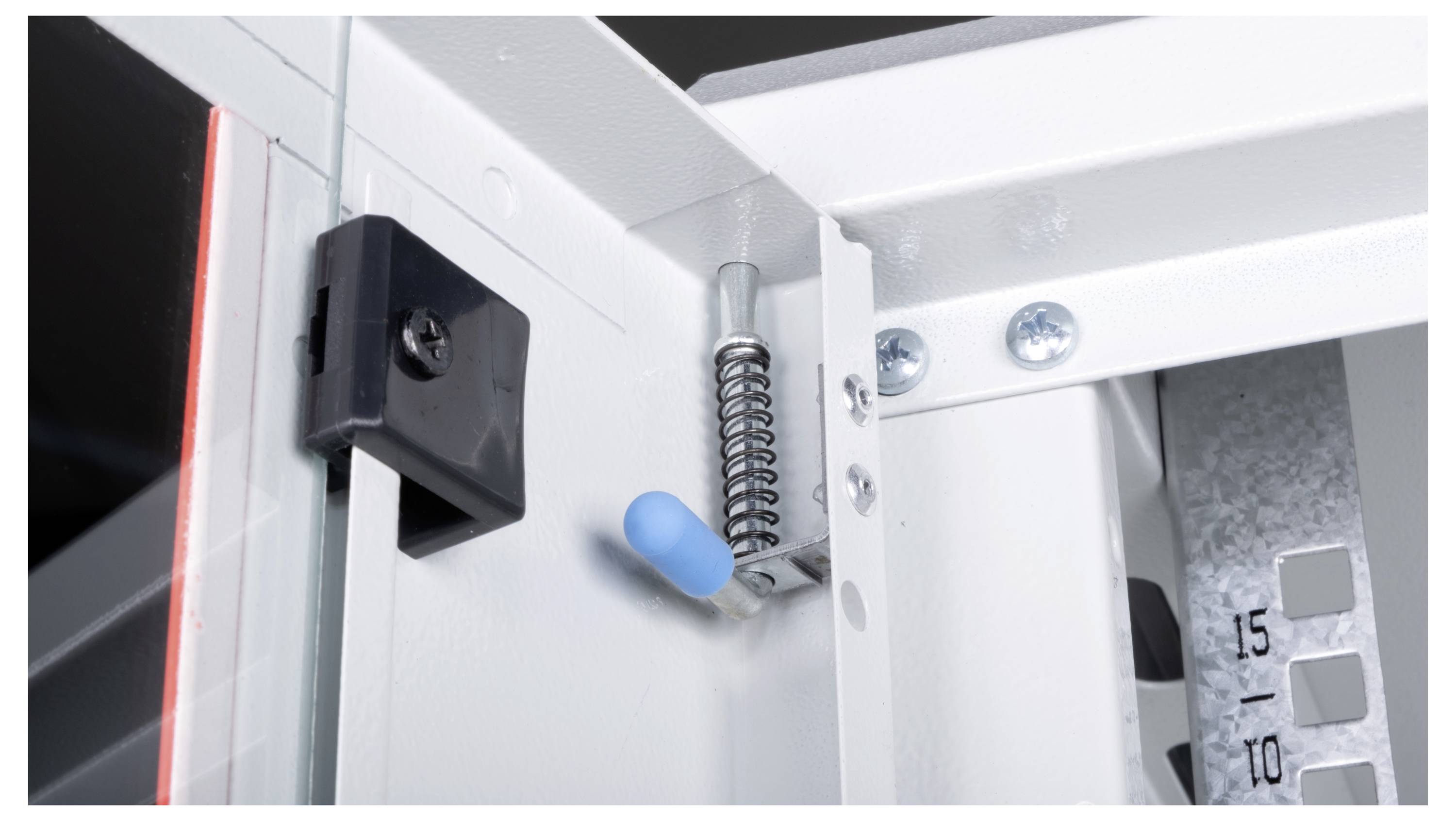 Mechanizm wewnętrzny drzwiczek szafki z niebieskim zatrzaskiem, zawiasą sprężynową oraz metalowymi elementami, prezentujący jego funkcję otwierania.