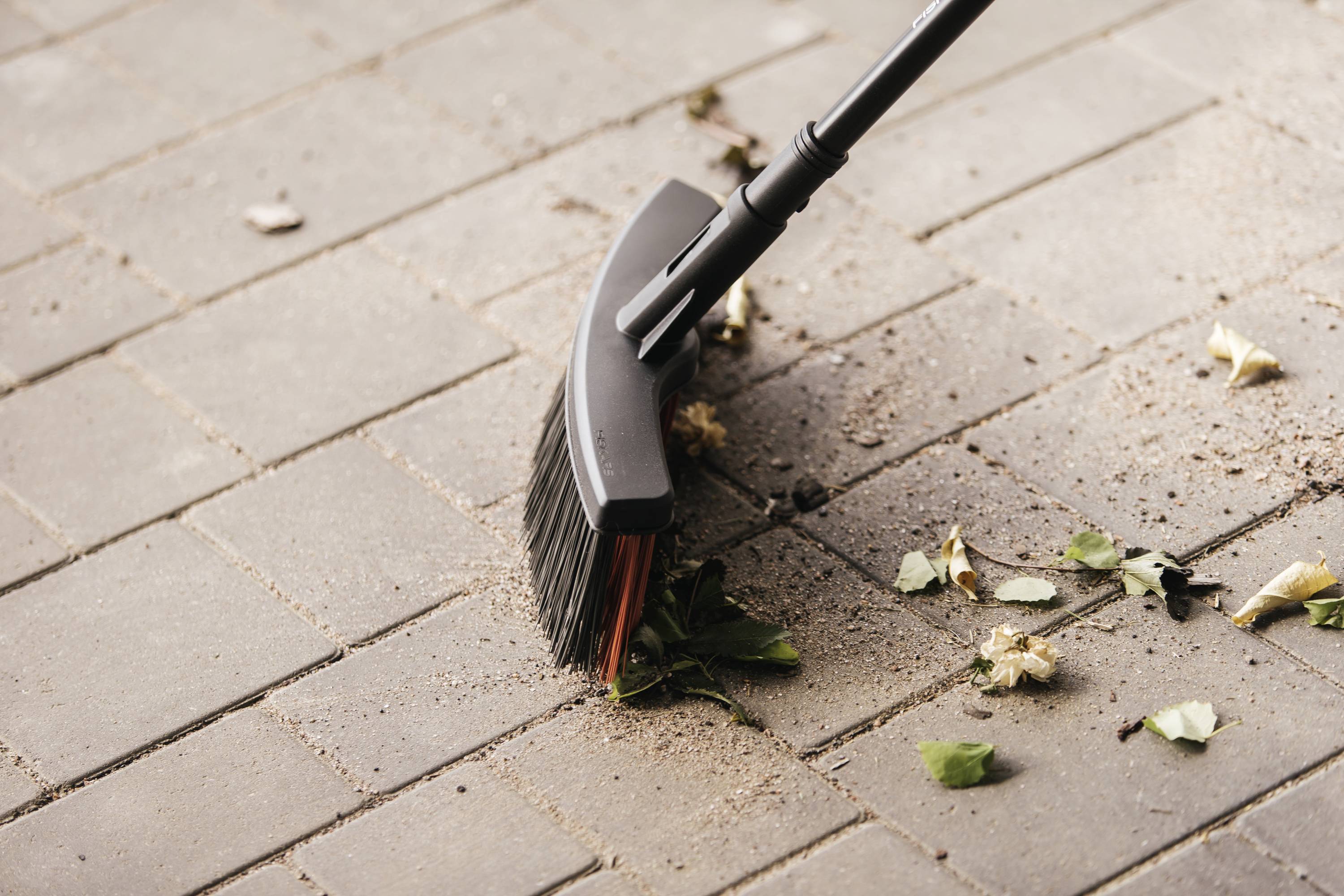 Miotła zamiata suche liście i brud na wybrukowanej powierzchni.