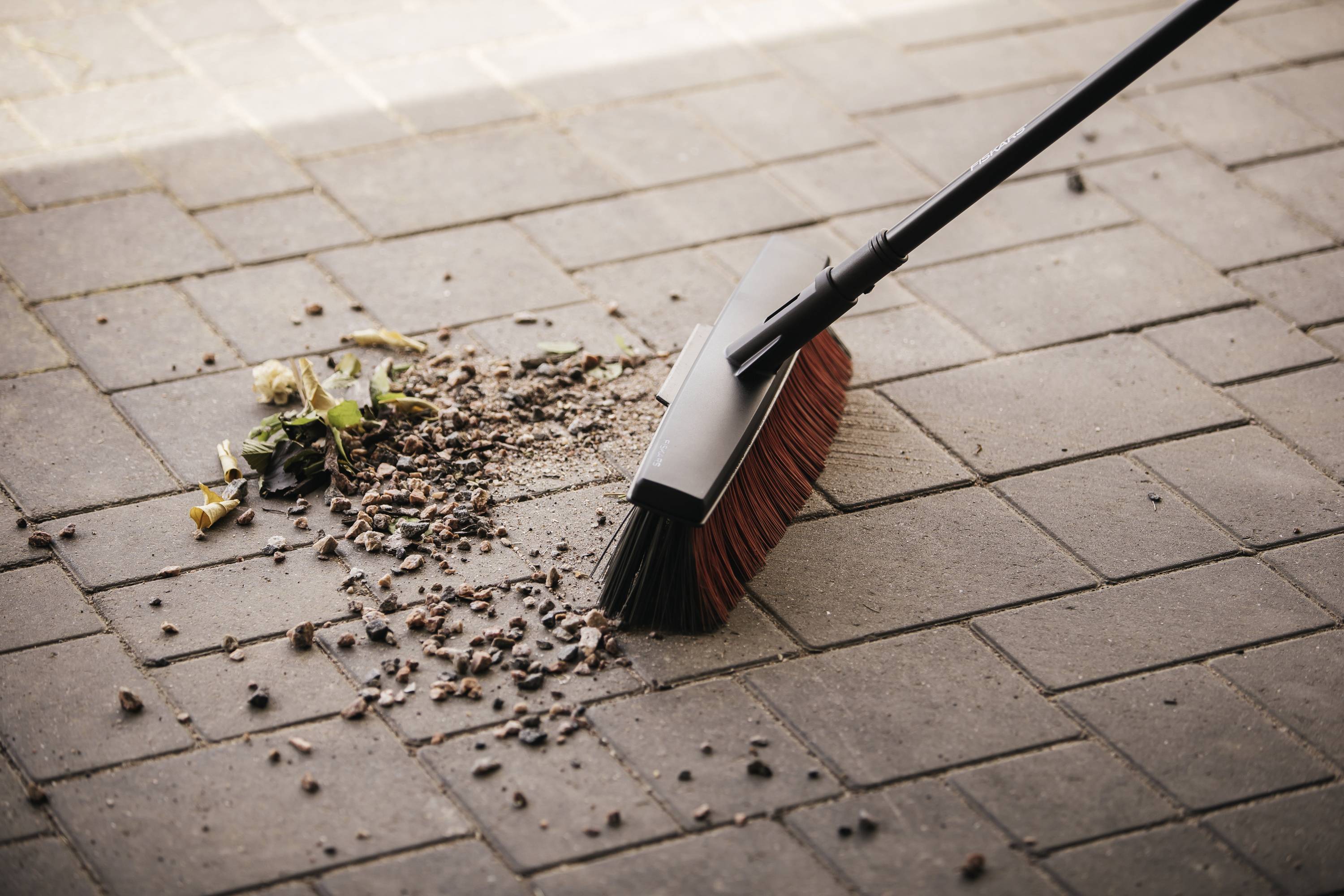 Ulica jest zamiatana miotłą. Na ziemi leżą liście i brud, które są zbierane.