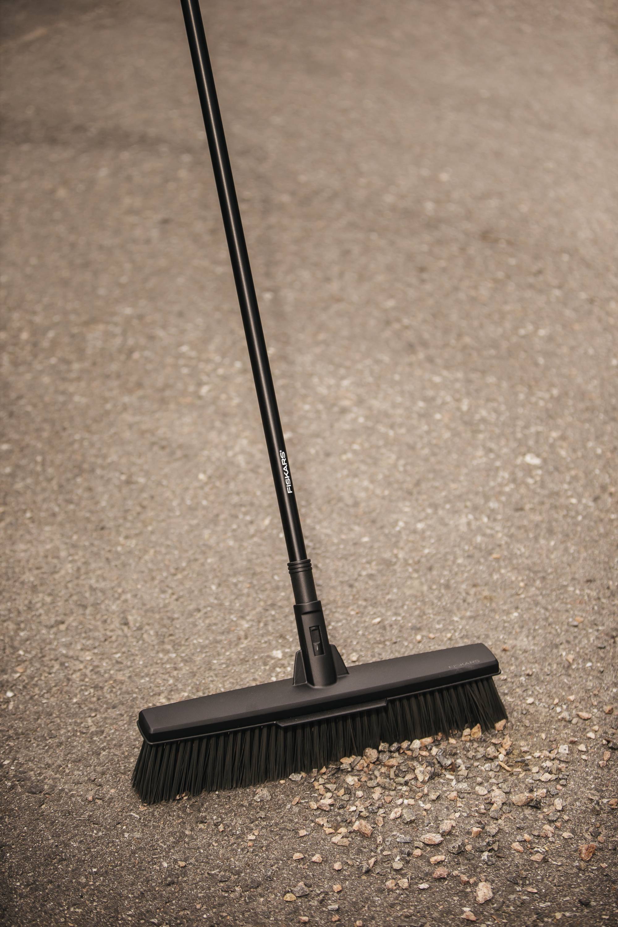 Czarny miotła zamiata liście i małe kamienie na asfaltowej powierzchni.