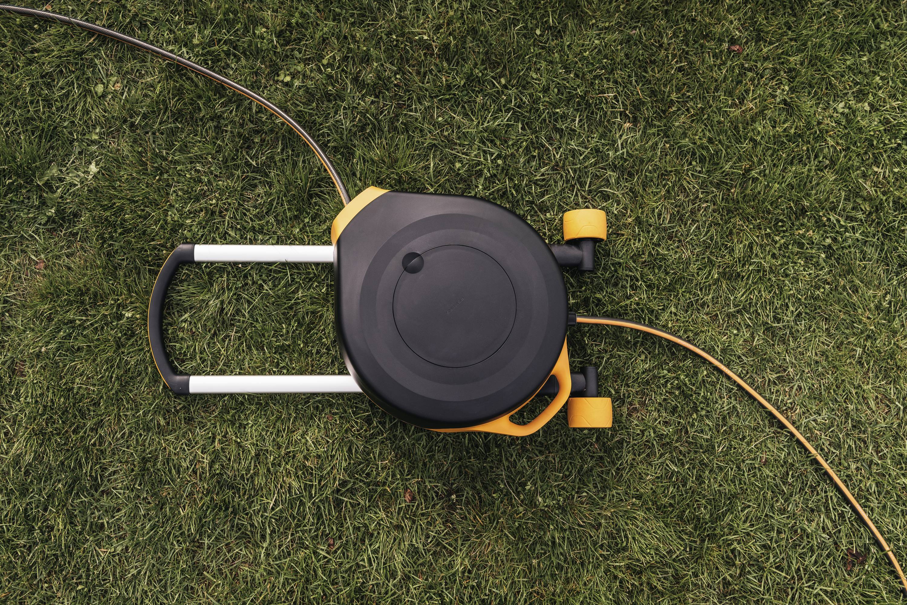 Kosiarka na zielonym trawniku widziana z góry; pomarańczowy kabel zwinięty; gotowa do pielęgnacji trawnika.
