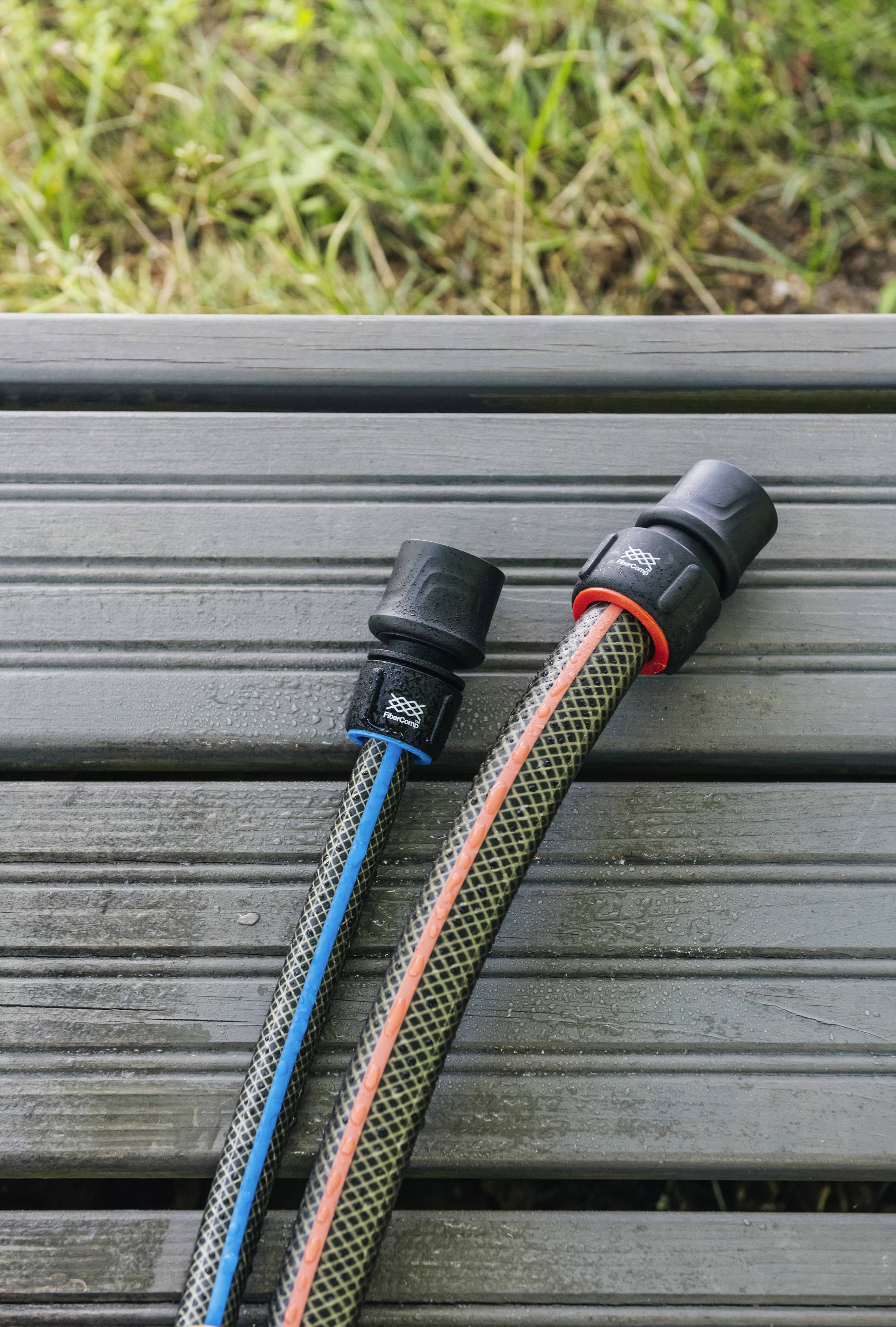 Dwa węże ogrodowe z plastikowymi złączkami leżą równolegle na drewnianej ławce. Jeden ma niebieskie oznaczenia, drugi czerwone.