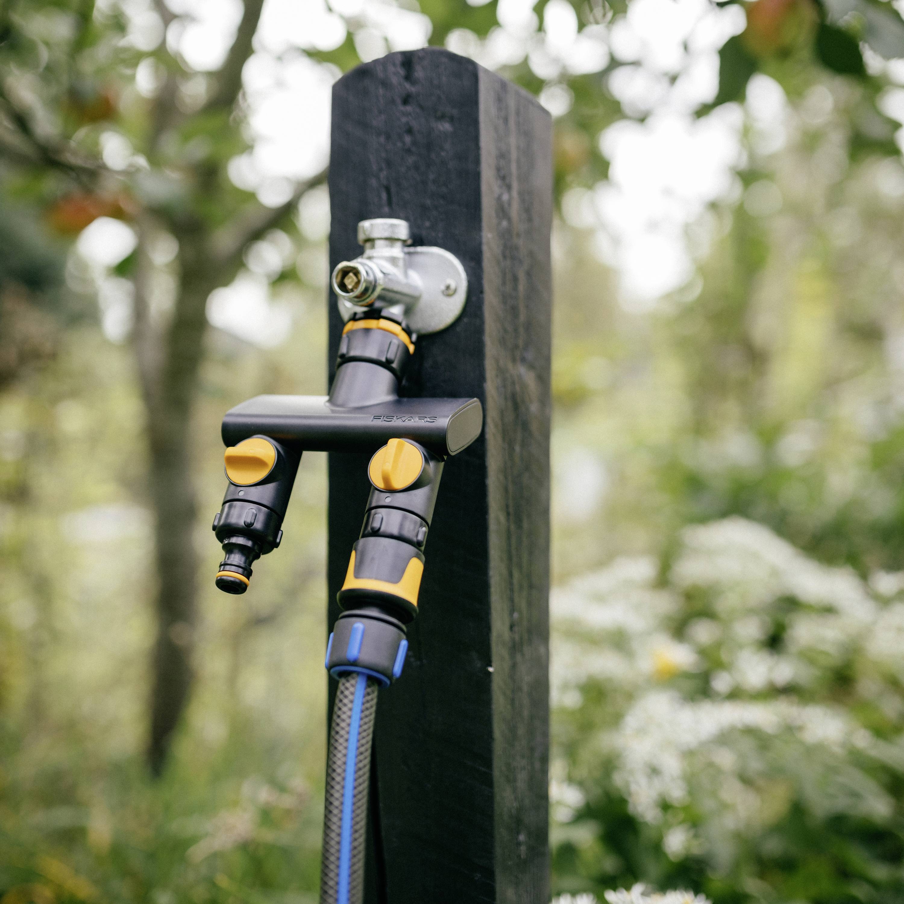 Wąż ogrodowy przymocowany do czarnego drewnianego słupa, gotowy do podlewania ogrodu. Zielone, naturalne tło.