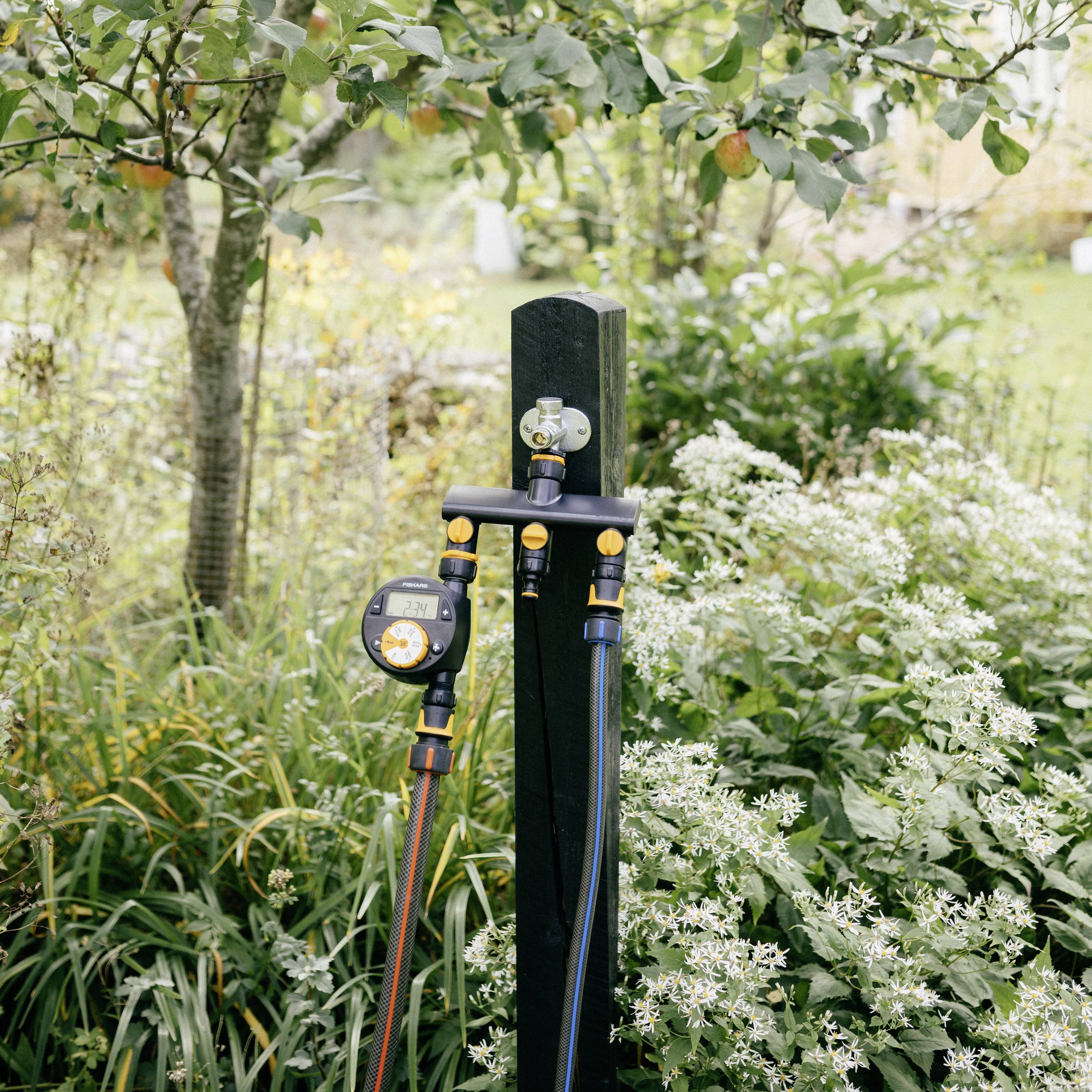 Zielony krajobraz ogrodowy z systemem nawadniania zamontowanym na słupie. W tle widoczne są drzewa i krzewy.