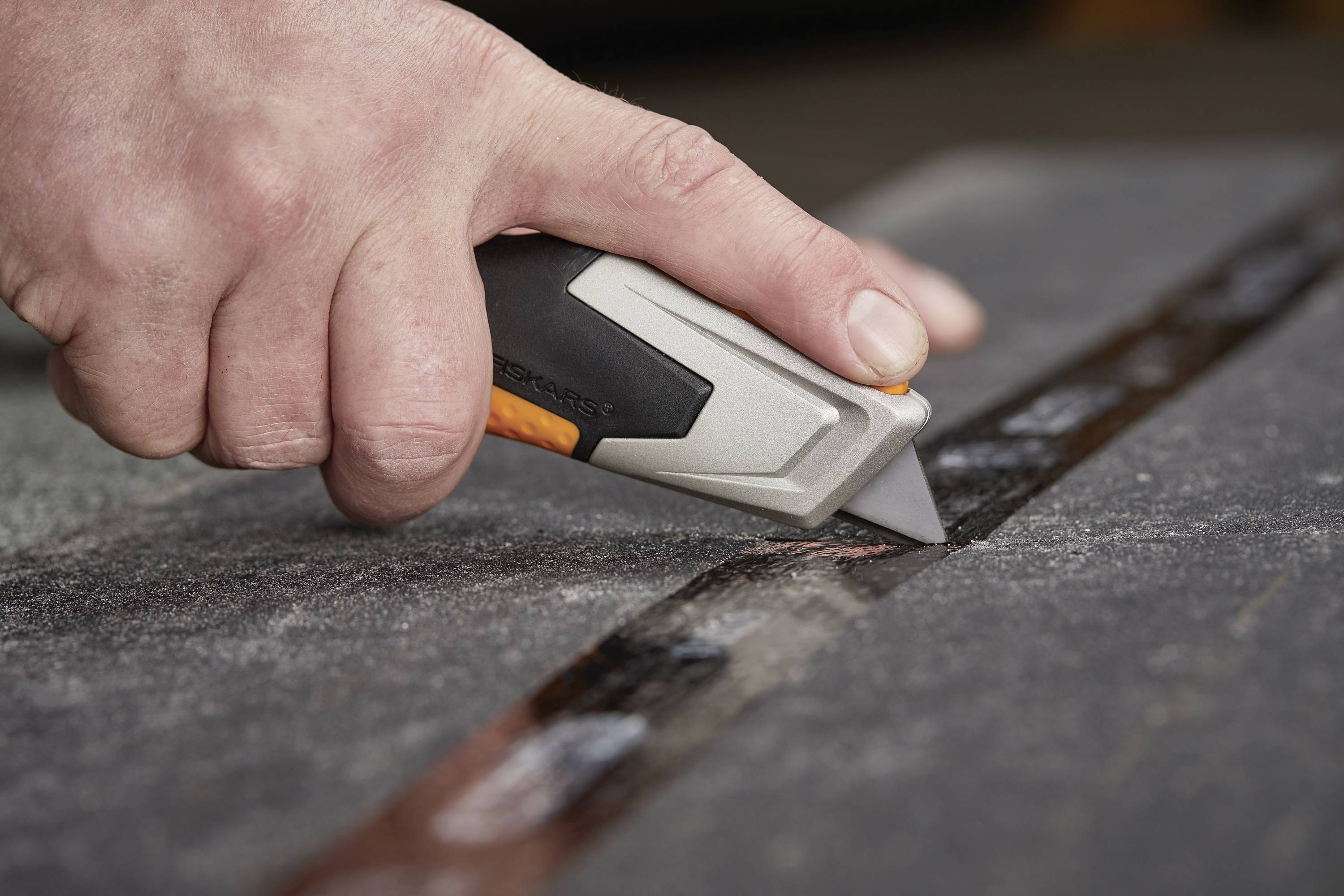 Jedna ręka trzyma nóż do dywanów i przecina prostą linię w ciemnej tkaninie lub wykładzinie.