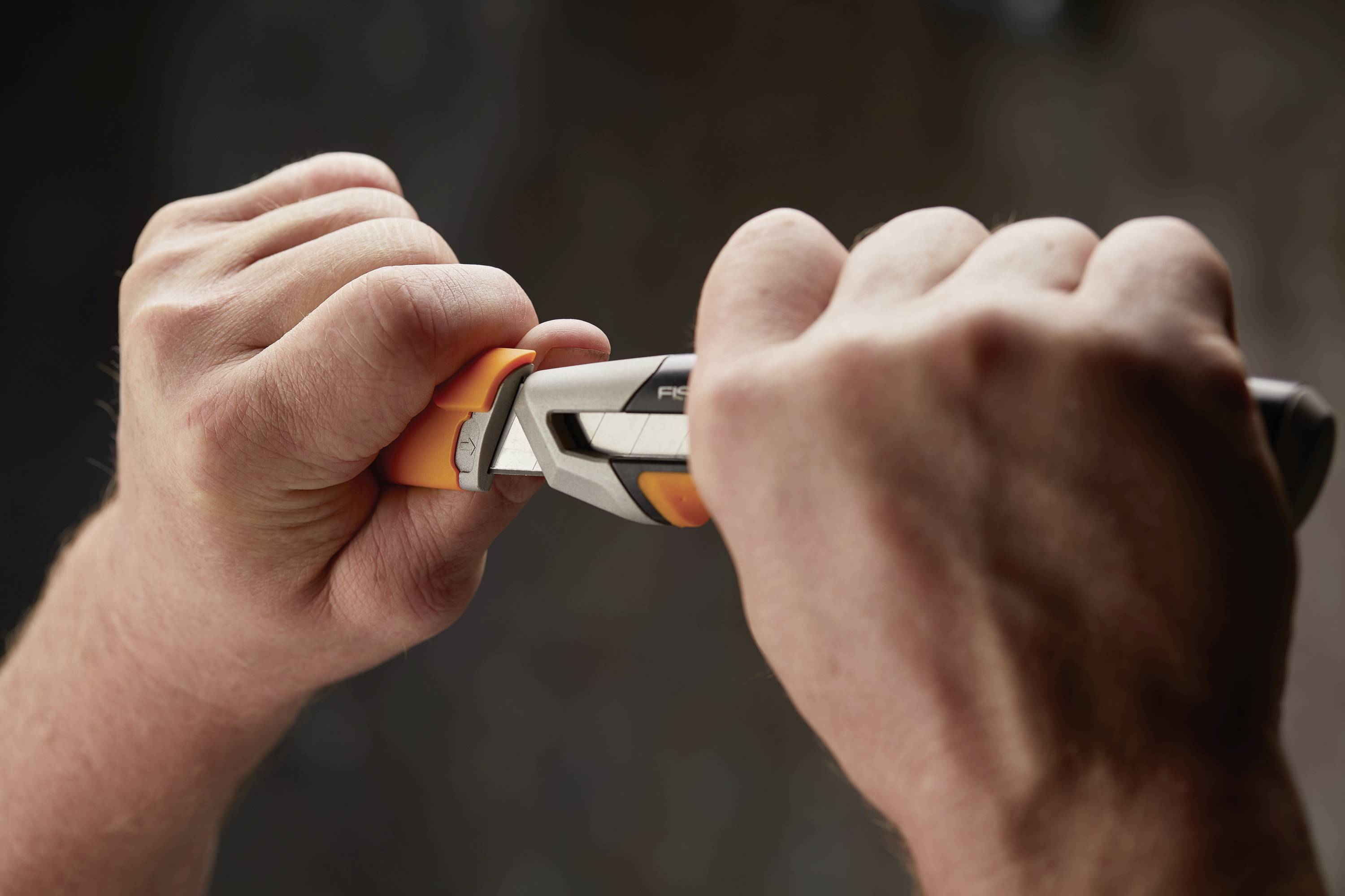 Dwie ręce używają szczypiec do trzymania pomarańczowego elementu. Tło jest rozmyte.