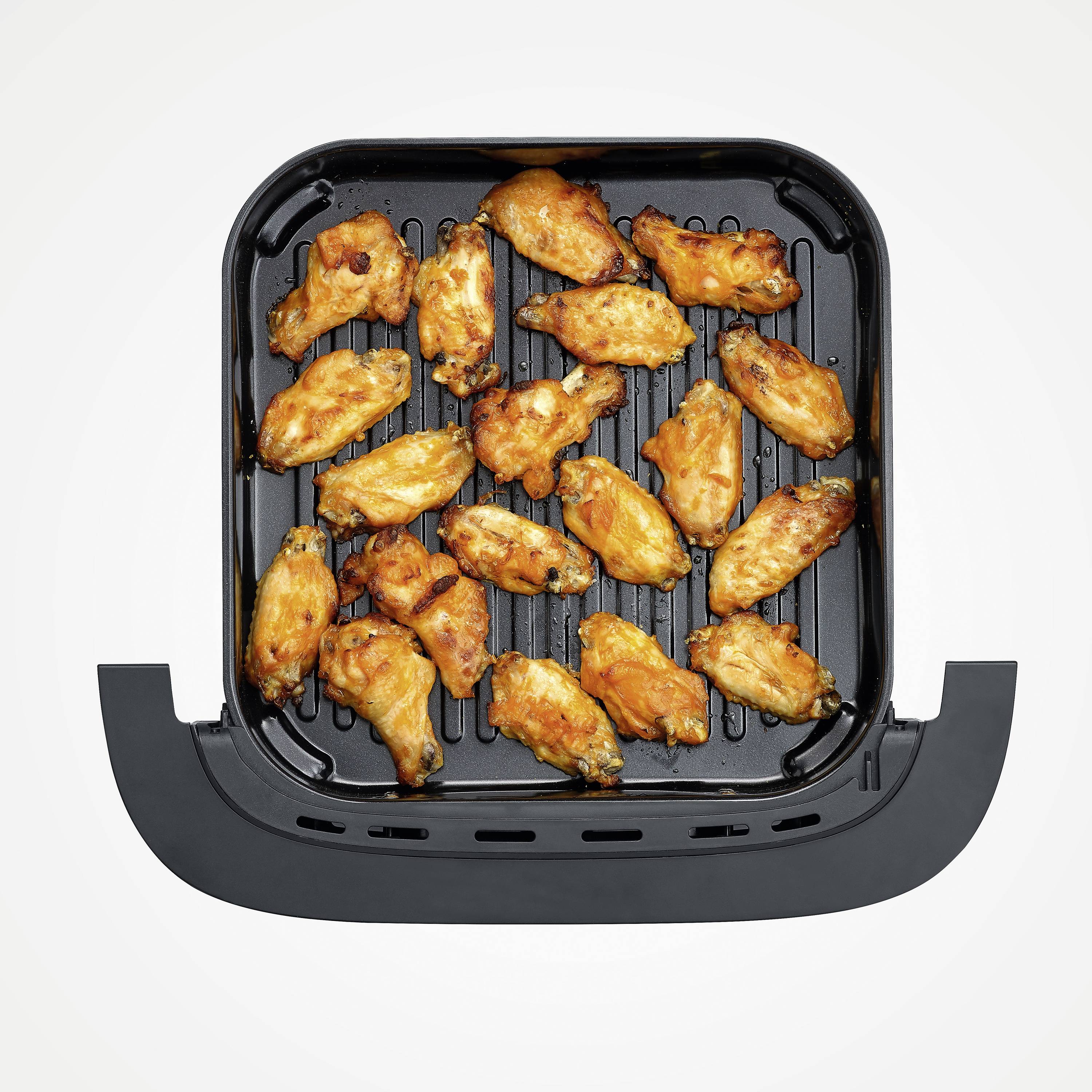 Skrzydełka z kurczaka, złoto-brązowe, równomiernie ułożone w koszu air fryer.