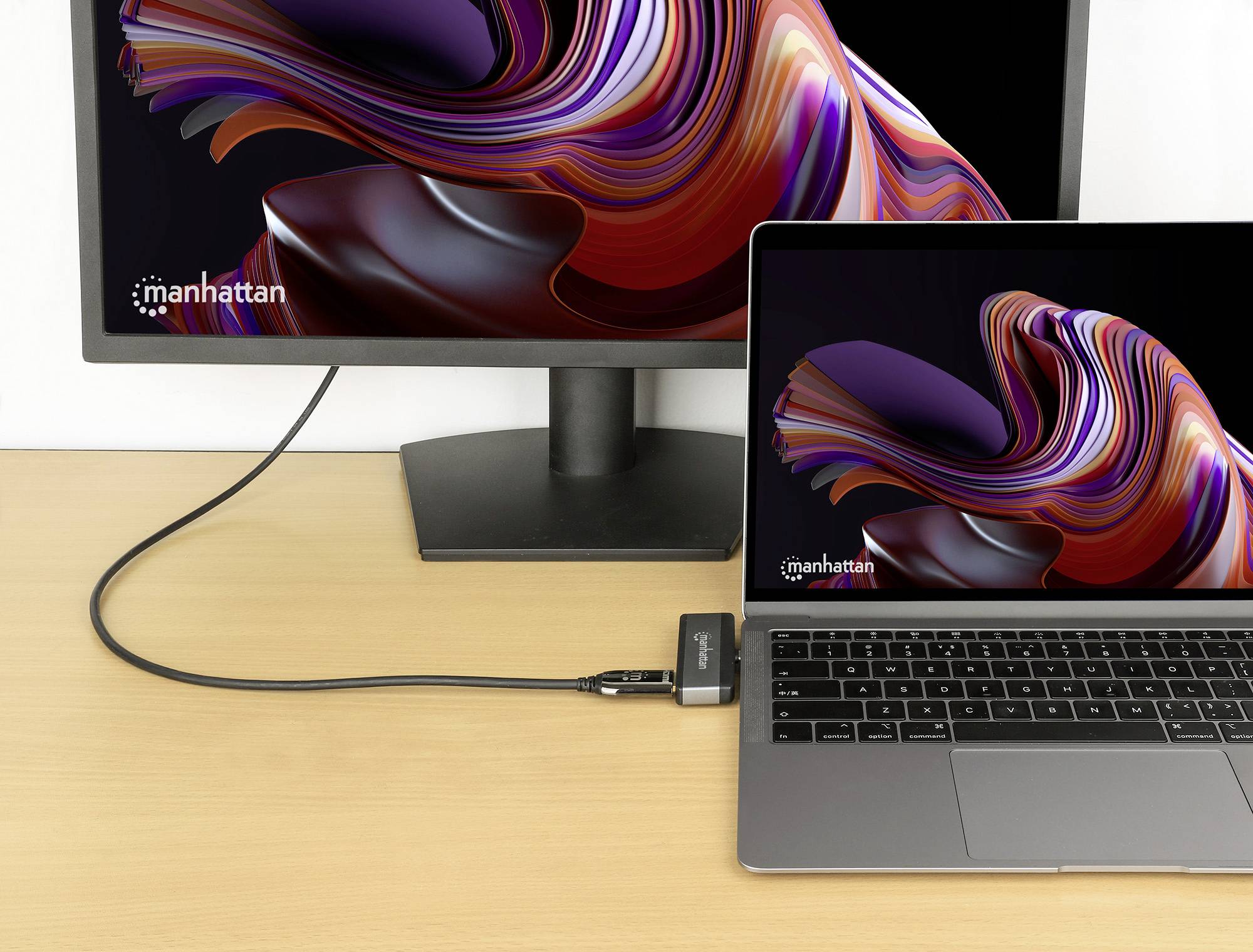 Laptop i外置显示器，配有相同的抽象图形，通过黑色电缆连接在木桌上。