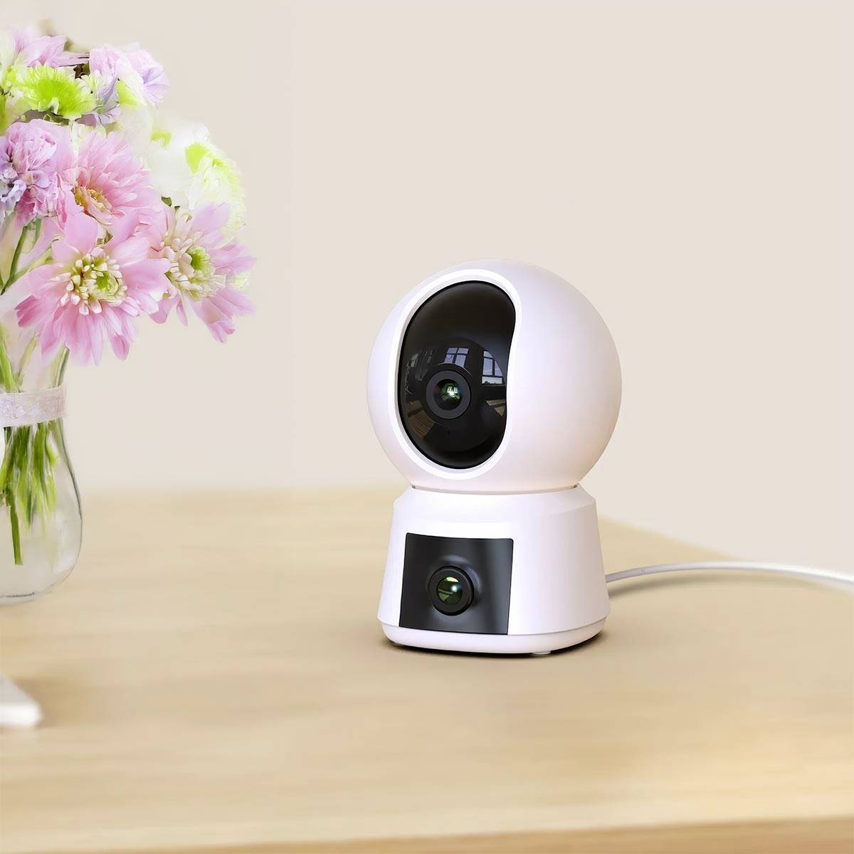 Nowoczesna, biała kamera monitorująca stoi na drewnianym stole obok bukietu kwiatów w szklanym wazonie.