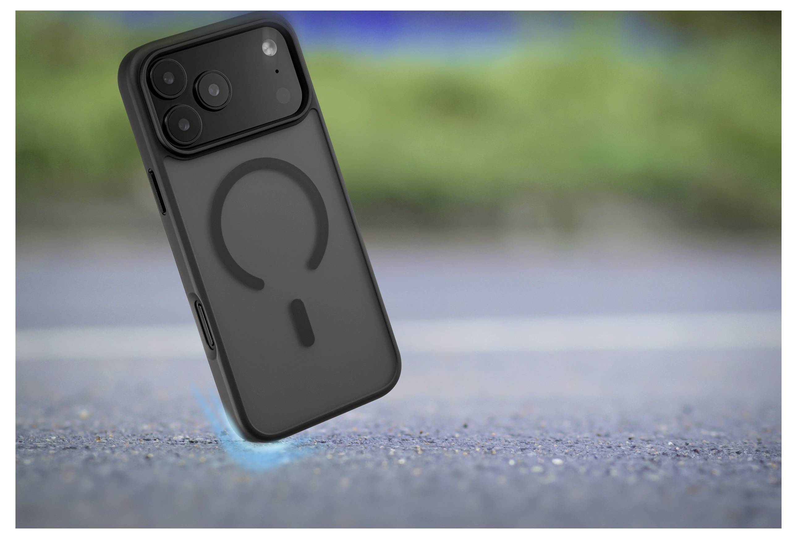 Czarny smartfon z unikalnym wzorem obiektywu i widocznym symbolem ładowania na obudowie, unoszący się nad rozmytą powierzchnią na wolnym powietrzu.
