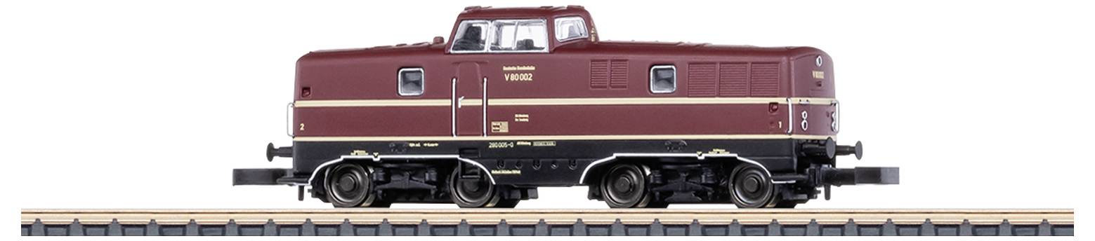 Ciemnoczerwona lokomotywa modelowa w skali H0 stoi na odcinku torów. Posiada żółte i czarne detale i wygląda na bardzo szczegółowo wykonaną.