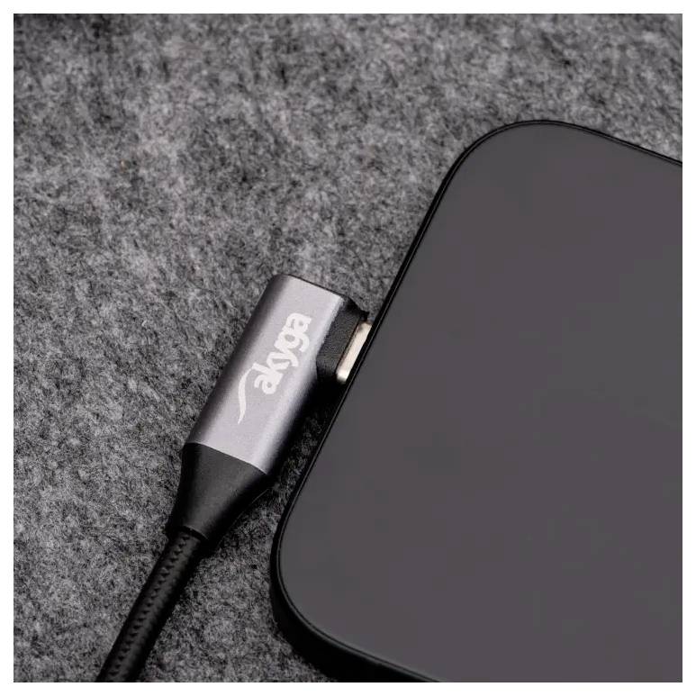 Szary telefon leży na szarej powierzchni, podłączony do czarnego kabla ładującego marki 'ENET'.