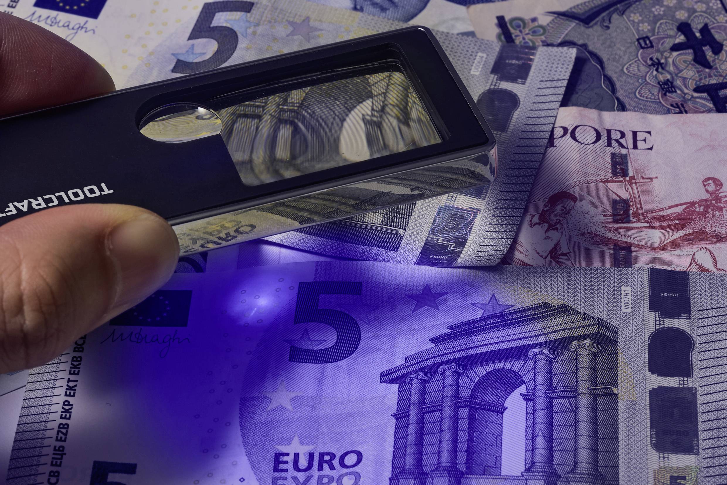 Banknoty euro poddawane inspekcji przy użyciu światła ultrafioletowego, ujawniające cechy zabezpieczające, takie jak hologramy i znaki wodne.