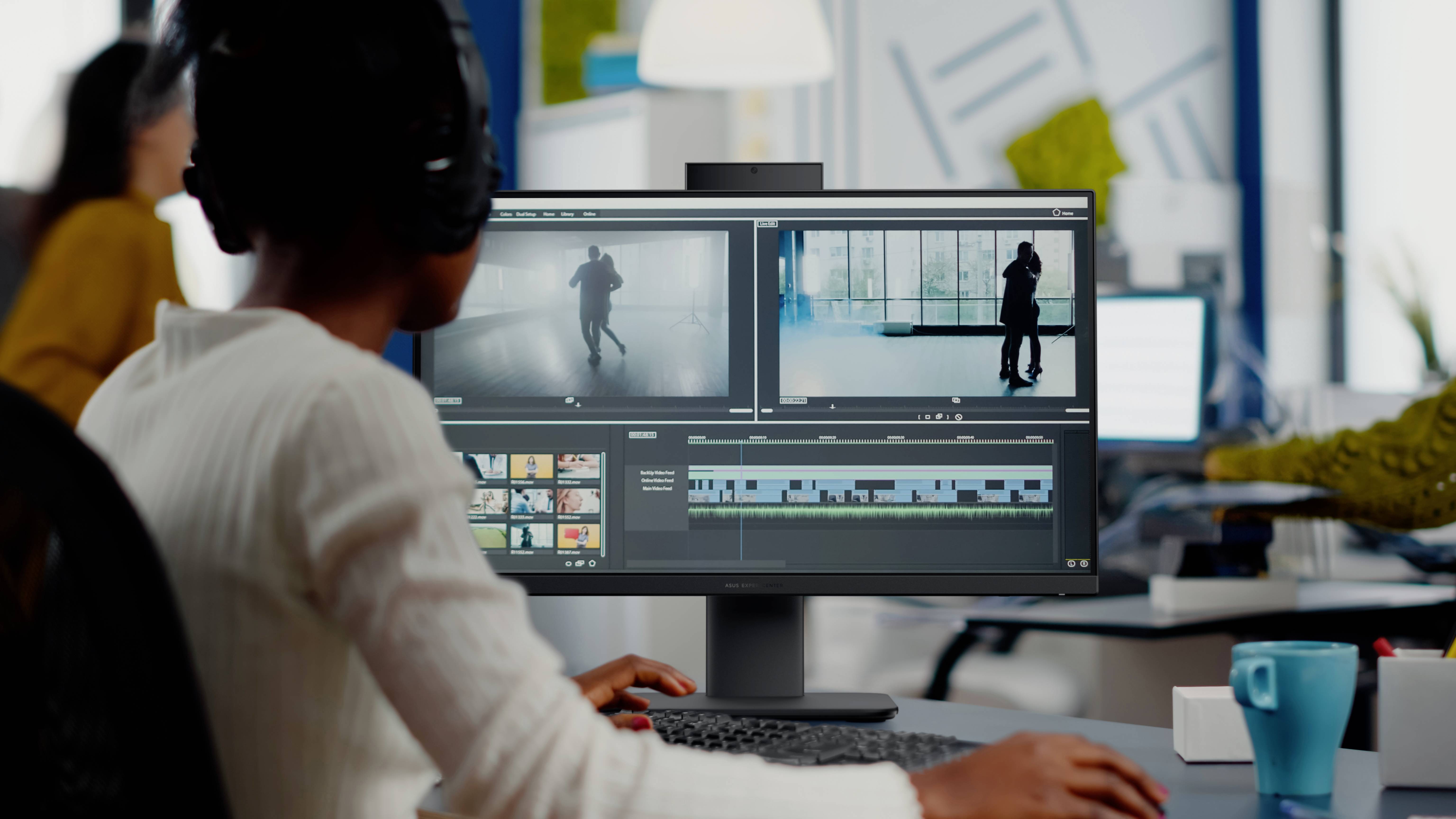 Osoba w słuchawkach montuje materiał wideo na komputerze w biurowym otoczeniu. Na ekranie widoczna jest oś czasu i klipy podglądu.