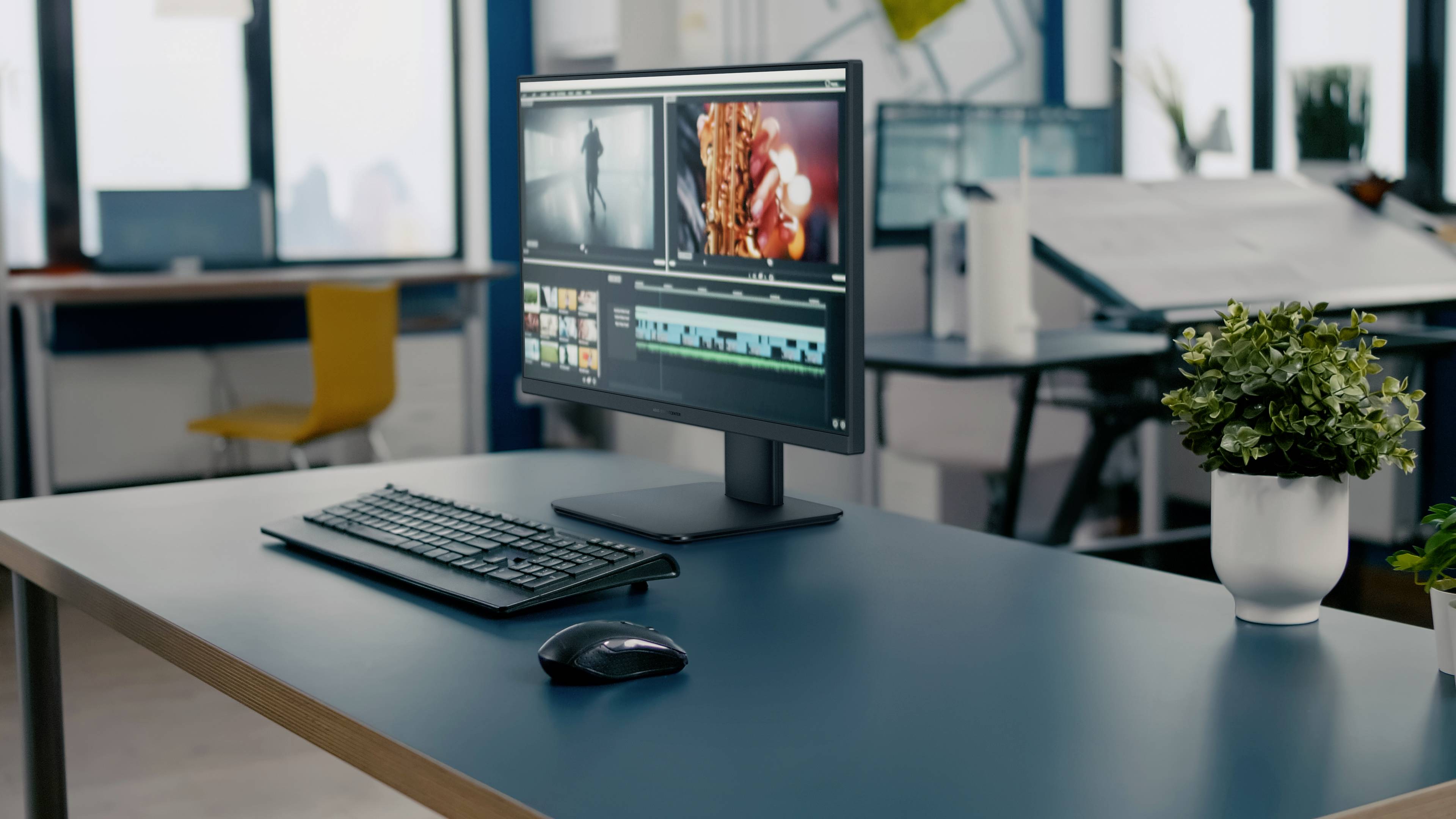 Monitor komputerowy na biurku wyświetla oprogramowanie do edycji wideo z klipami. W pobliżu znajduje się klawiatura i mysz. W tle widoczne jest wnętrze biura.