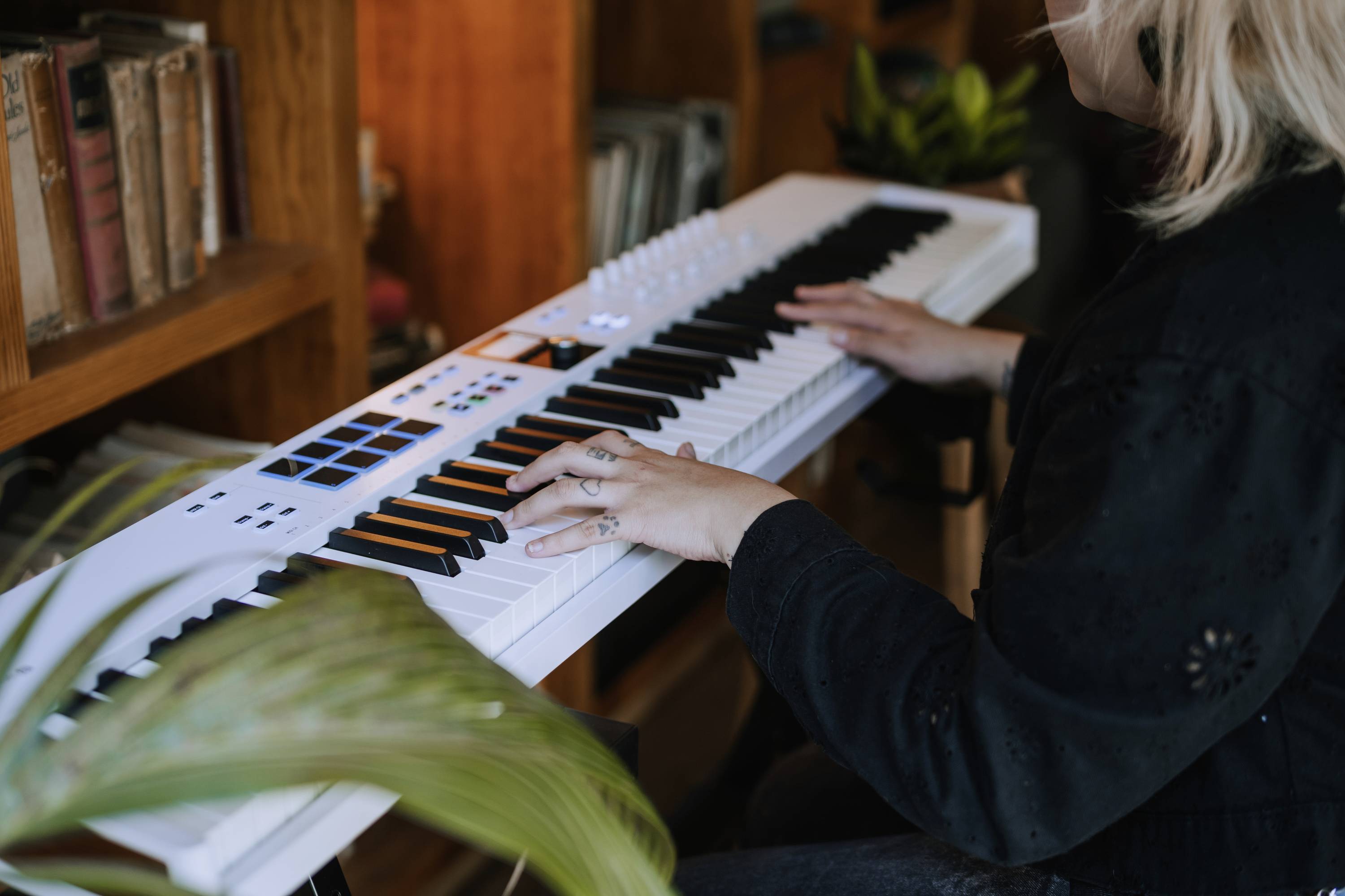Osoba gra na białym keyboardzie w przytulnym pokoju, otoczona książkami i roślinami.