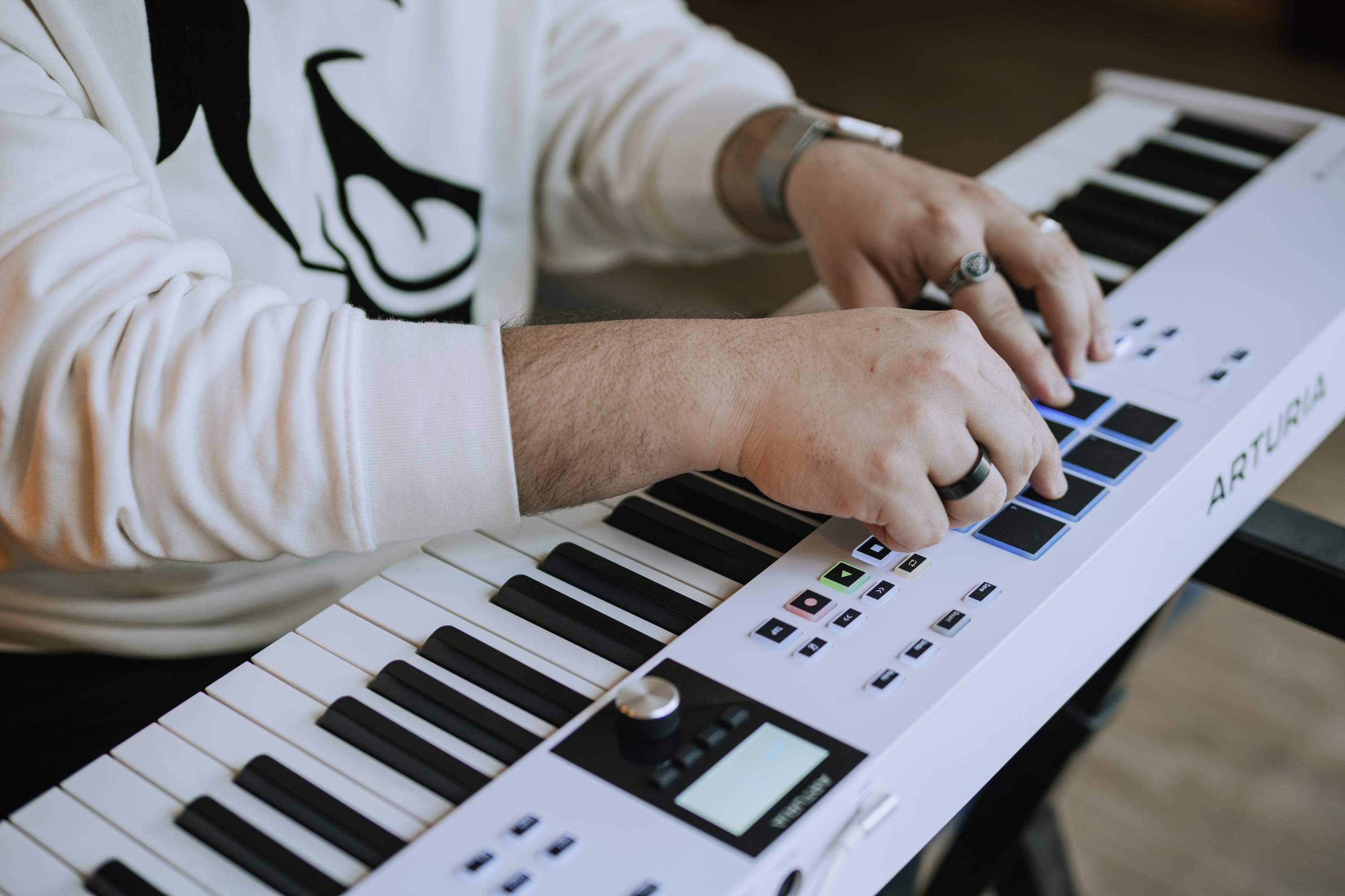 Osoba gra na białej klawiaturze z niebieskimi padami. Osoba ma na sobie biały sweter.