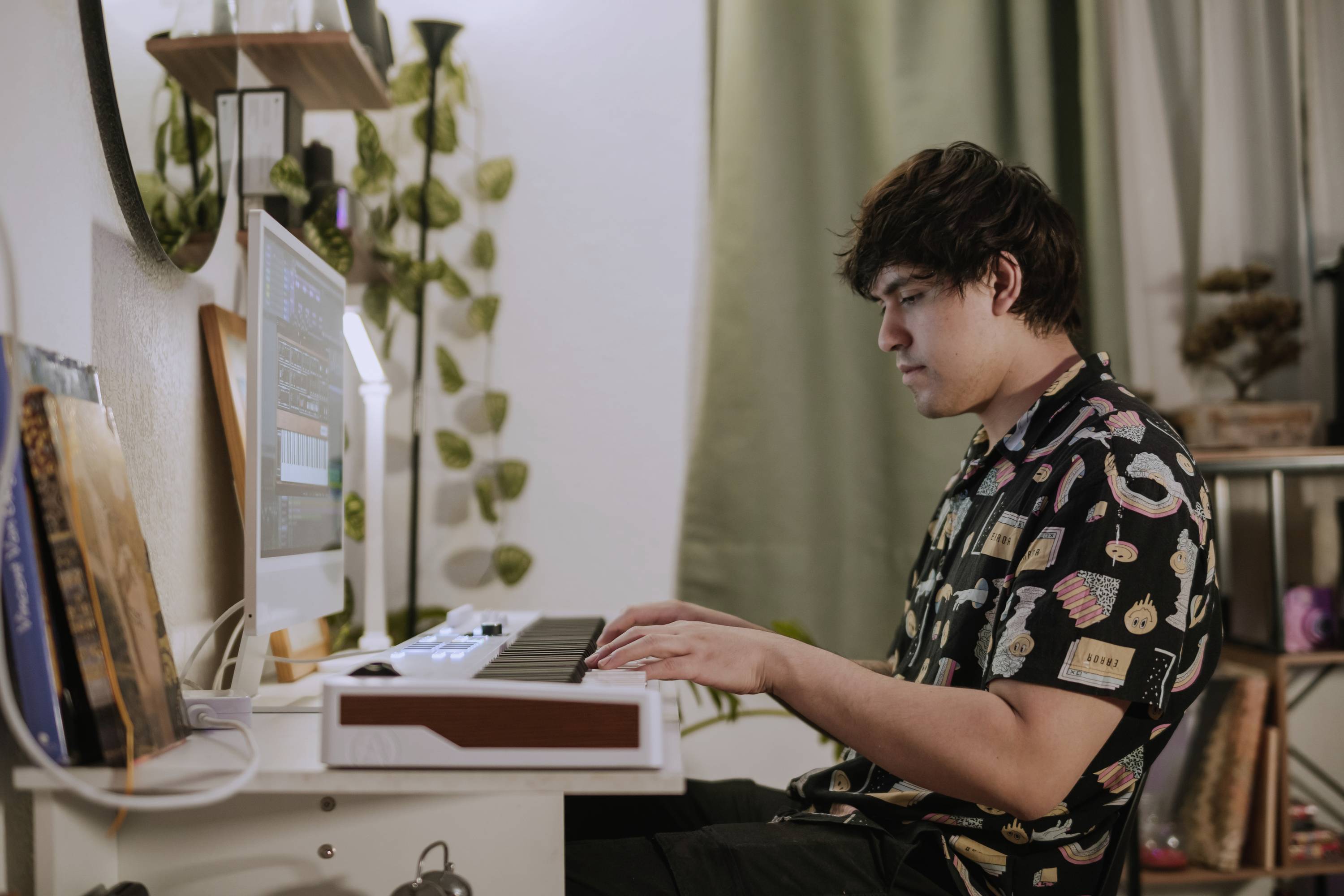 Osoba gra skoncentrowanie na elektrycznym keyboardzie przy biurku w przytulnie urządzonym pokoju.