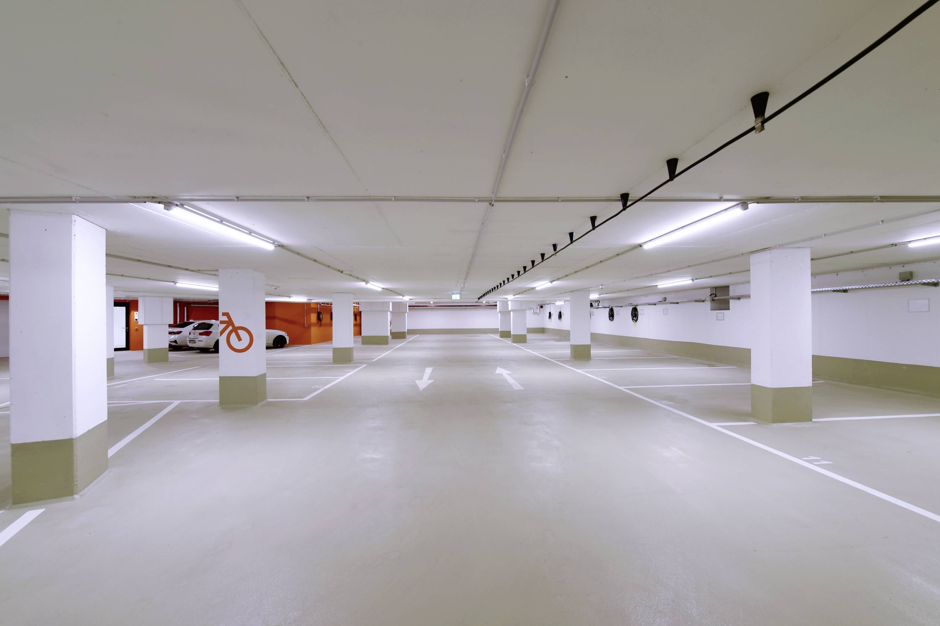 Pusty, oświetlony parking w garażu wielopoziomowym ze strzałkami na podłodze wskazującymi kierunek jazdy.
