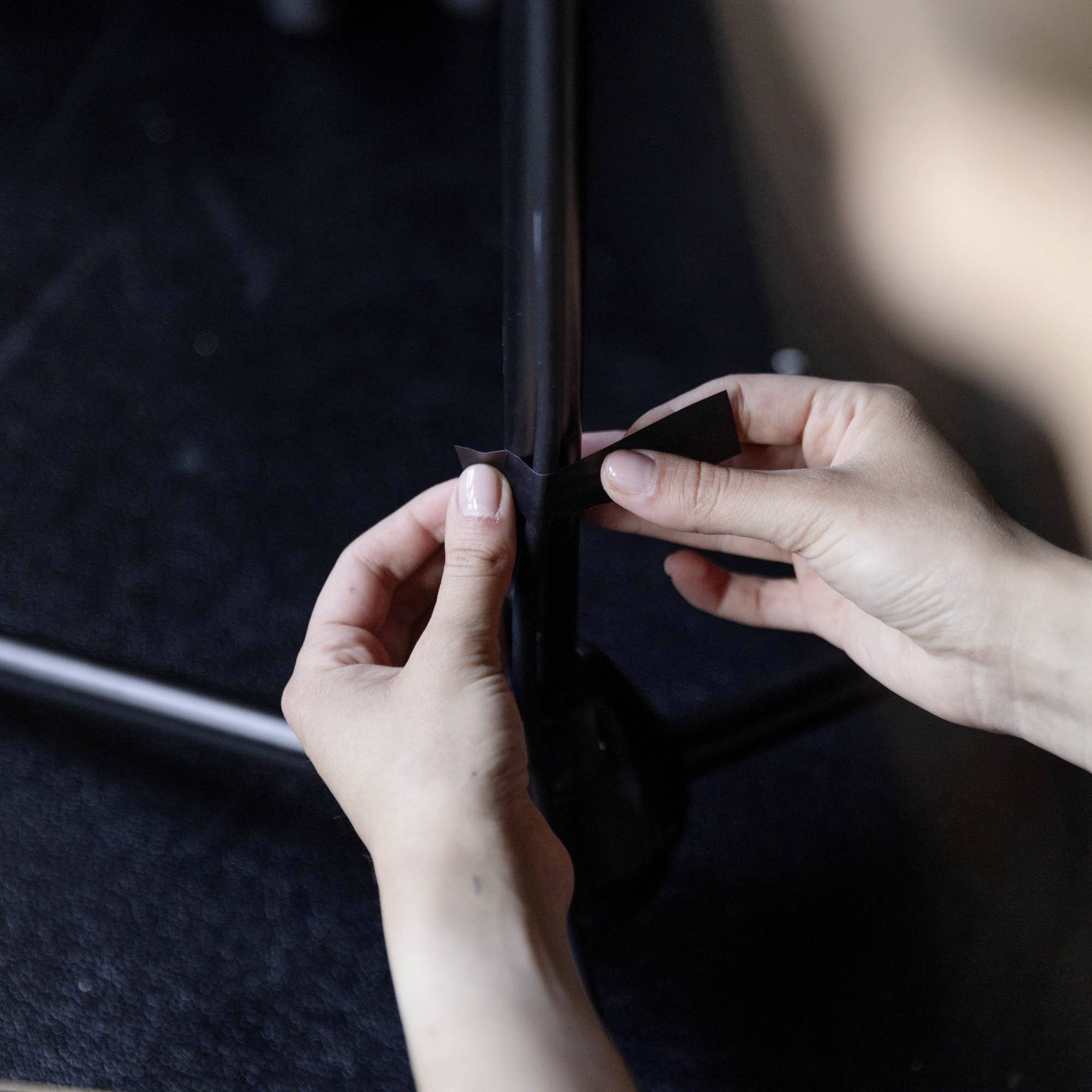 Osoba przykleja rękami czarną taśmę klejącą wokół rury.