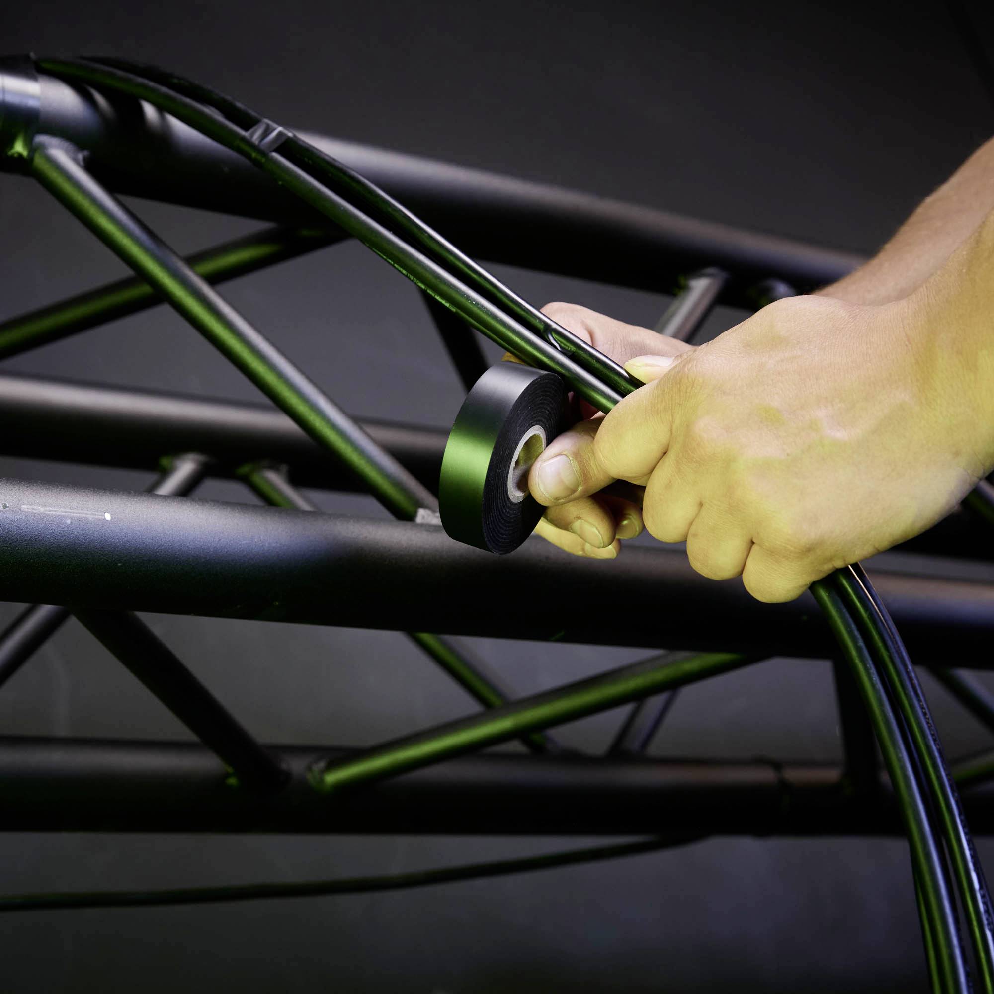 Zbliżenie dłoni mocującej czarne kable taśmą izolacyjną do czarnej metalowej sztangi.