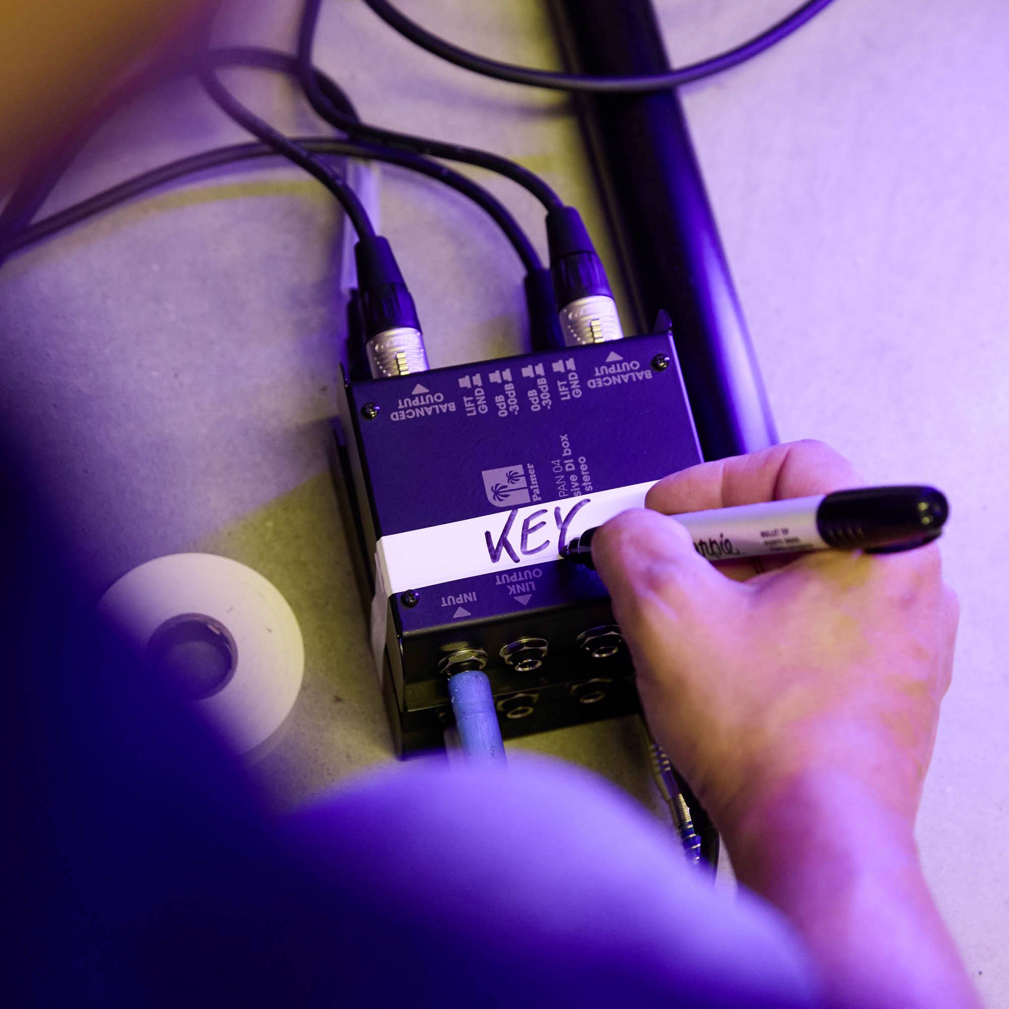 Zbliżenie pokazuje dłoń łączącą czarny kabel z urządzeniem. Widoczna naklejka na nim nosi napis 'KEY'.