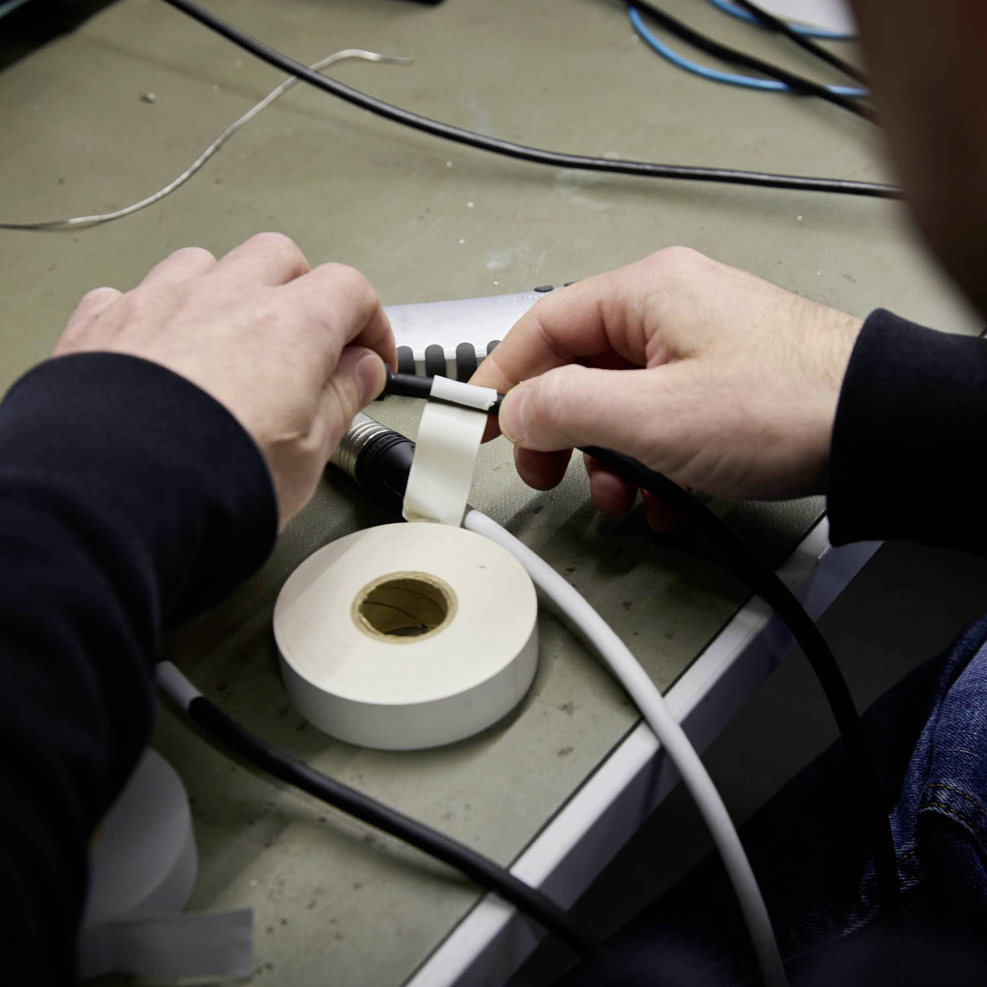 Osoba przykleja białą taśmę wokół kabla na stole. Obok leży rolka z podobną taśmą.