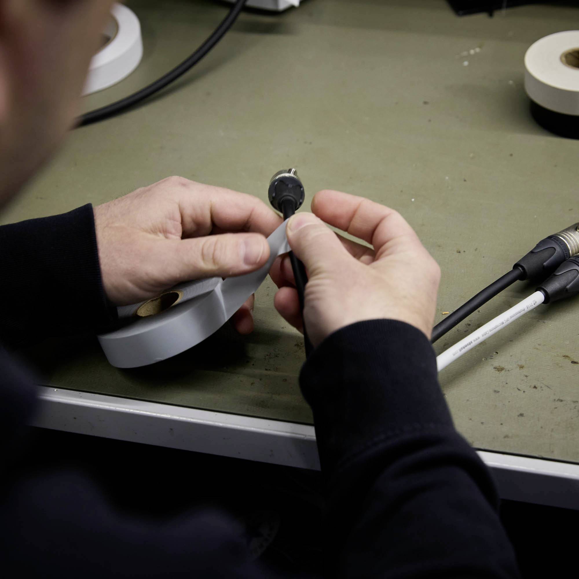 Osoba trzyma kabel i element łączący. Skupienie jest na obsłudze komponentów elektrycznych na stole.