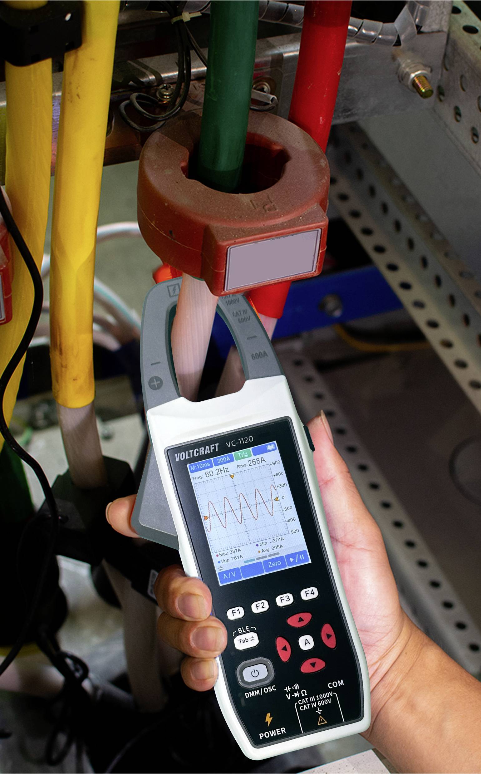 Technik mierzy natężenie prądu elektrycznego za pomocą ręcznego multimetru. Na ekranie wyświetla się falisty wzór, a urządzenie jest podłączone do przewodów.