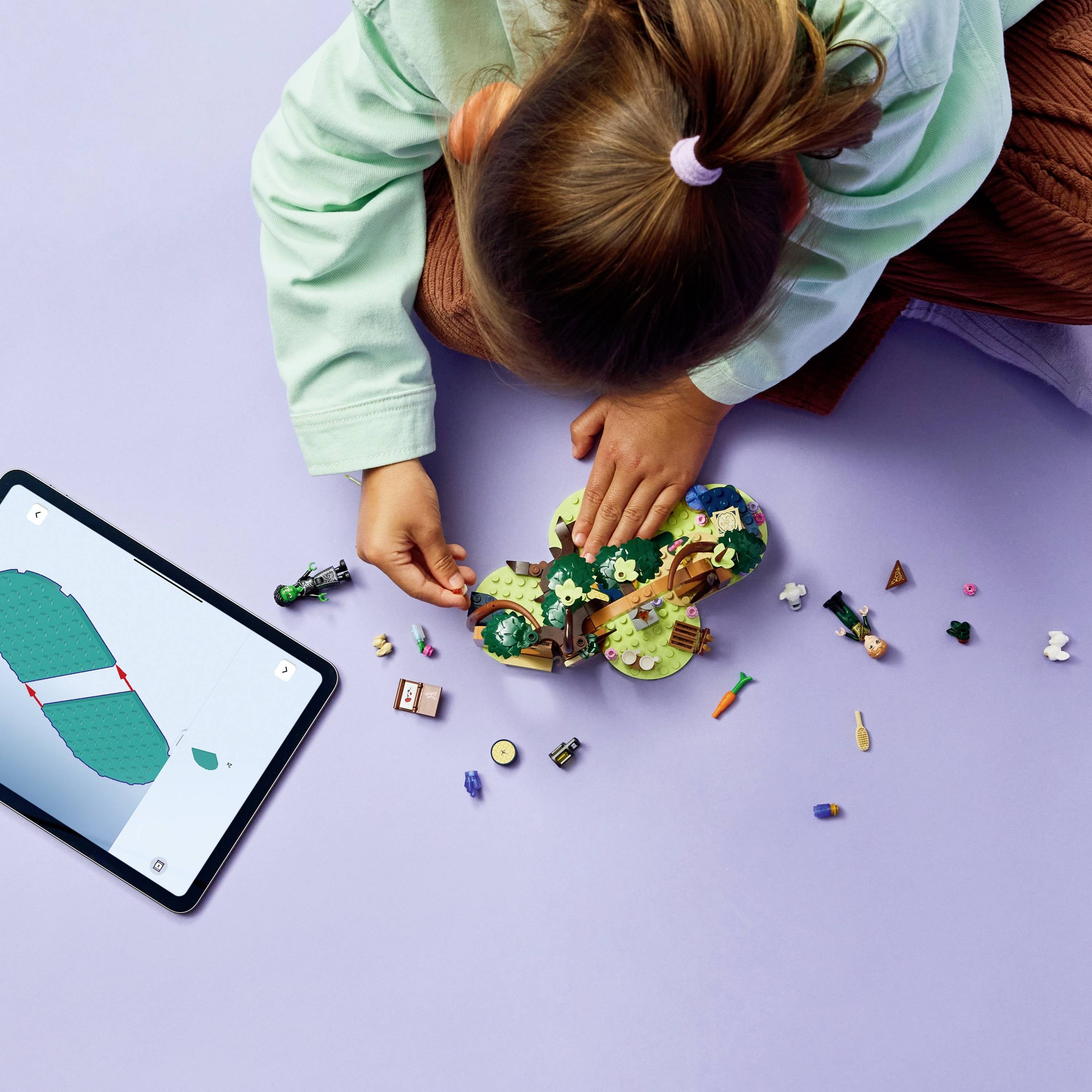 Dziecko bawi się kolorową figurką LEGO obok tabletu wyświetlającego ekran aplikacji do budowania LEGO, sugerując cyfrowe wsparcie podczas konstruowania.