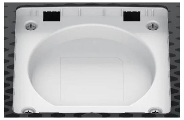 Kwadratowa puszka elektryczna z okrągłym wgłębieniem i czterema otworami na śruby na ciemnej, teksturowanej powierzchni.