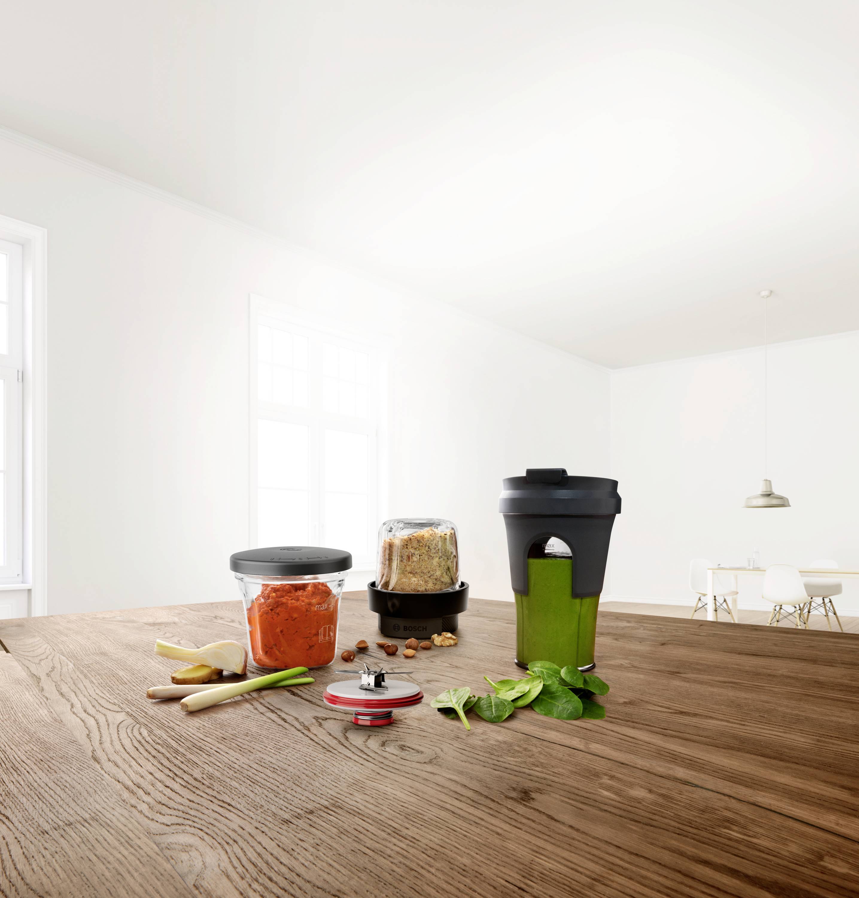 Na blacie kuchennym stoi blender z zielonym smoothie, druga słoiczek z czerwonym sosem, a w pobliżu leżą zioła, wszystko oświetlone jasnym, naturalnym światłem.