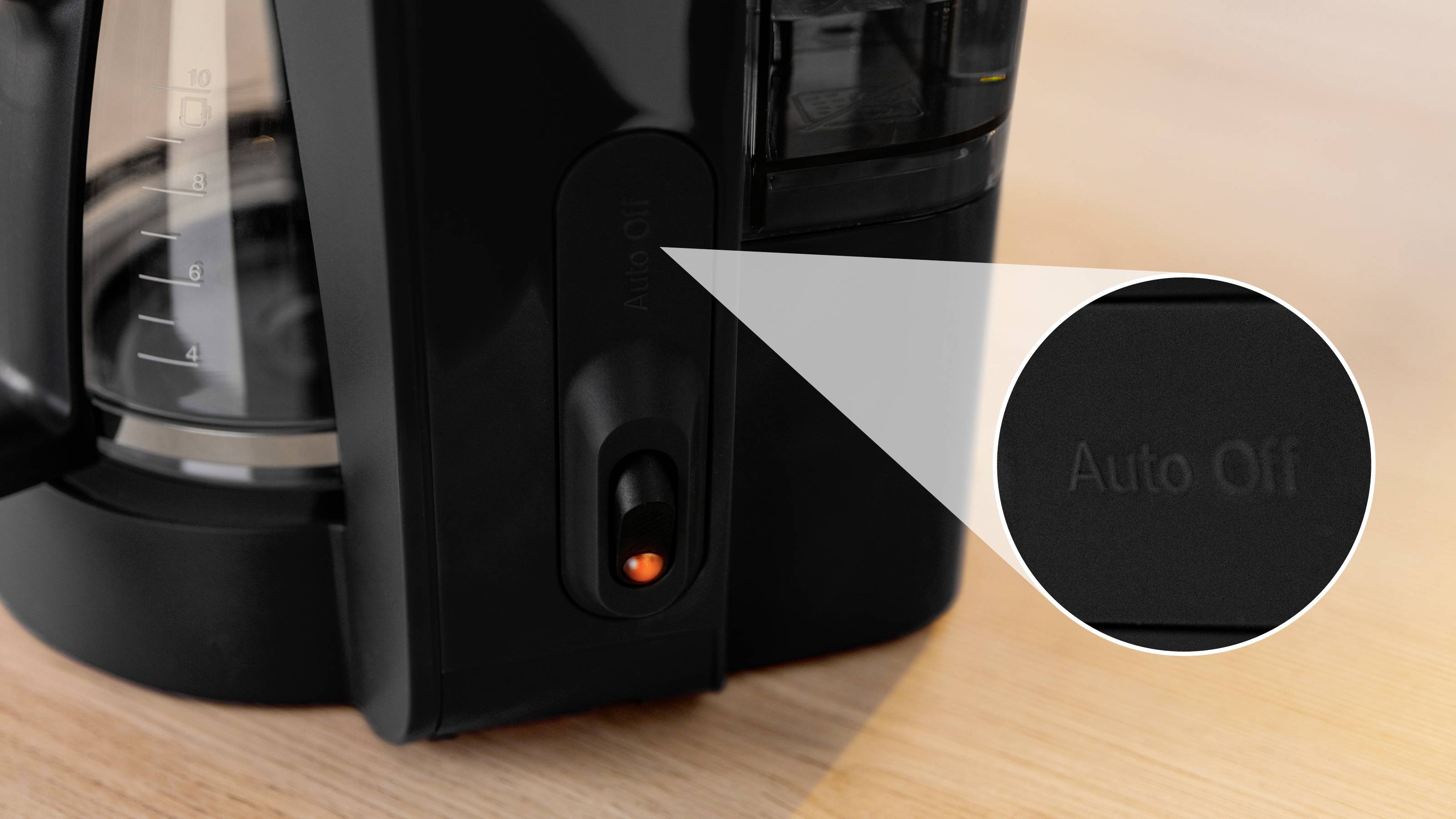 Zbliżenie ekspresu do kawy z podświetlonym przyciskiem 'Auto Off', podkreślającym funkcję automatycznego wyłączania, umieszczone na drewnianej powierzchni.