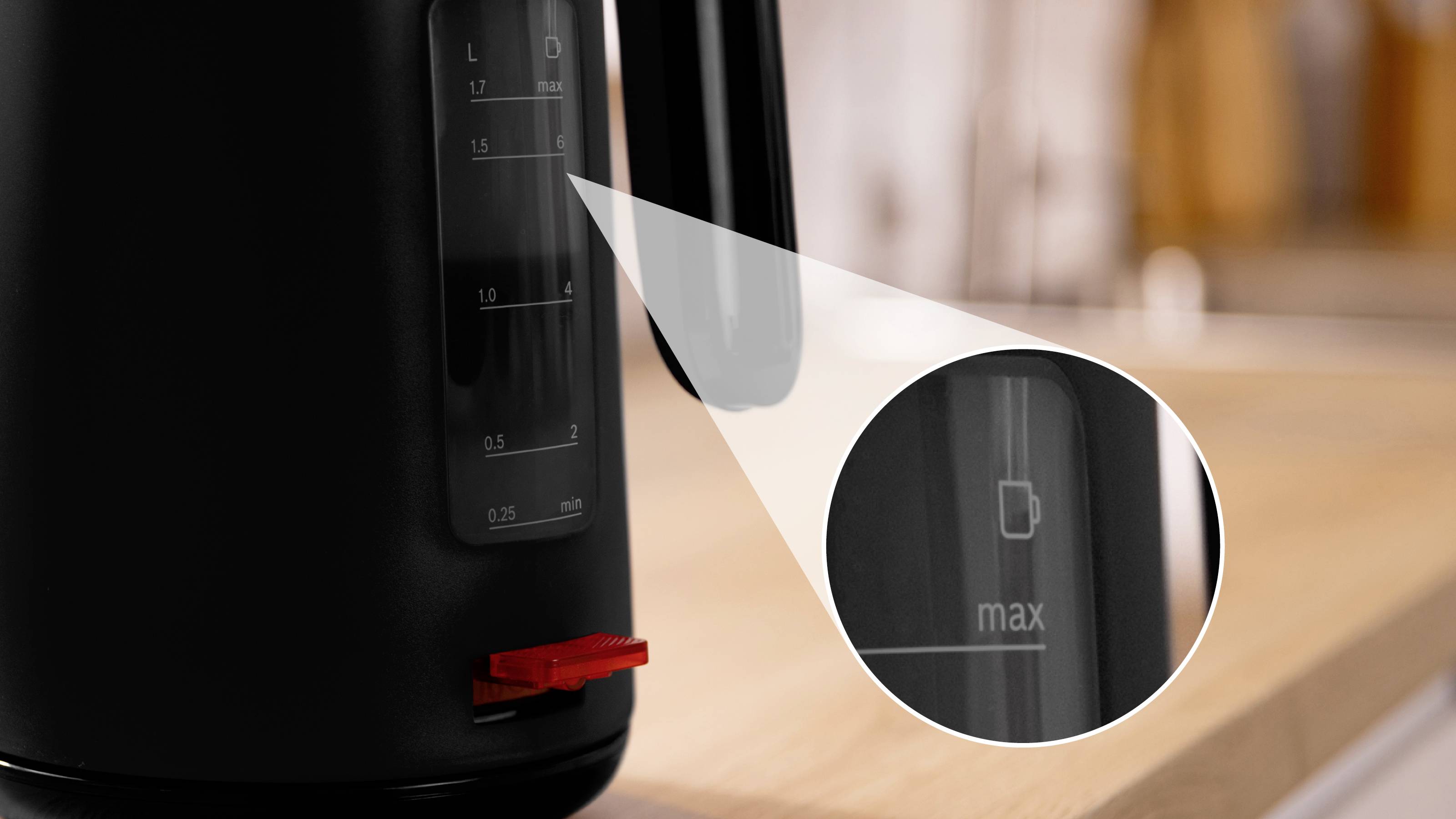 Czarny elektryczny czajnik z widocznym bliskim ujęciem wskaźnika poziomu wody, prezentujący maksymalną linię napełnienia, stojący na drewnianym blacie w kuchni.