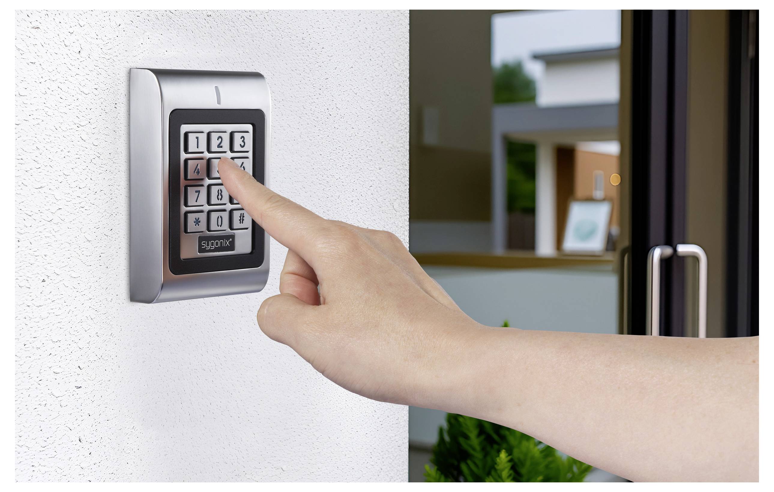 Dłoń naciska klawiaturę przy otwartych drzwiach, sugerując system zabezpieczeń lub kontroli dostępu w nowoczesnym budynku mieszkalnym.