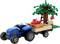 Niebieski zabawkowy traktor ciągnący przyczepę wypełnioną czerwonymi cegłami, obok zabawkowego drzewa z jabłkami i małej beżowej figurki psa.