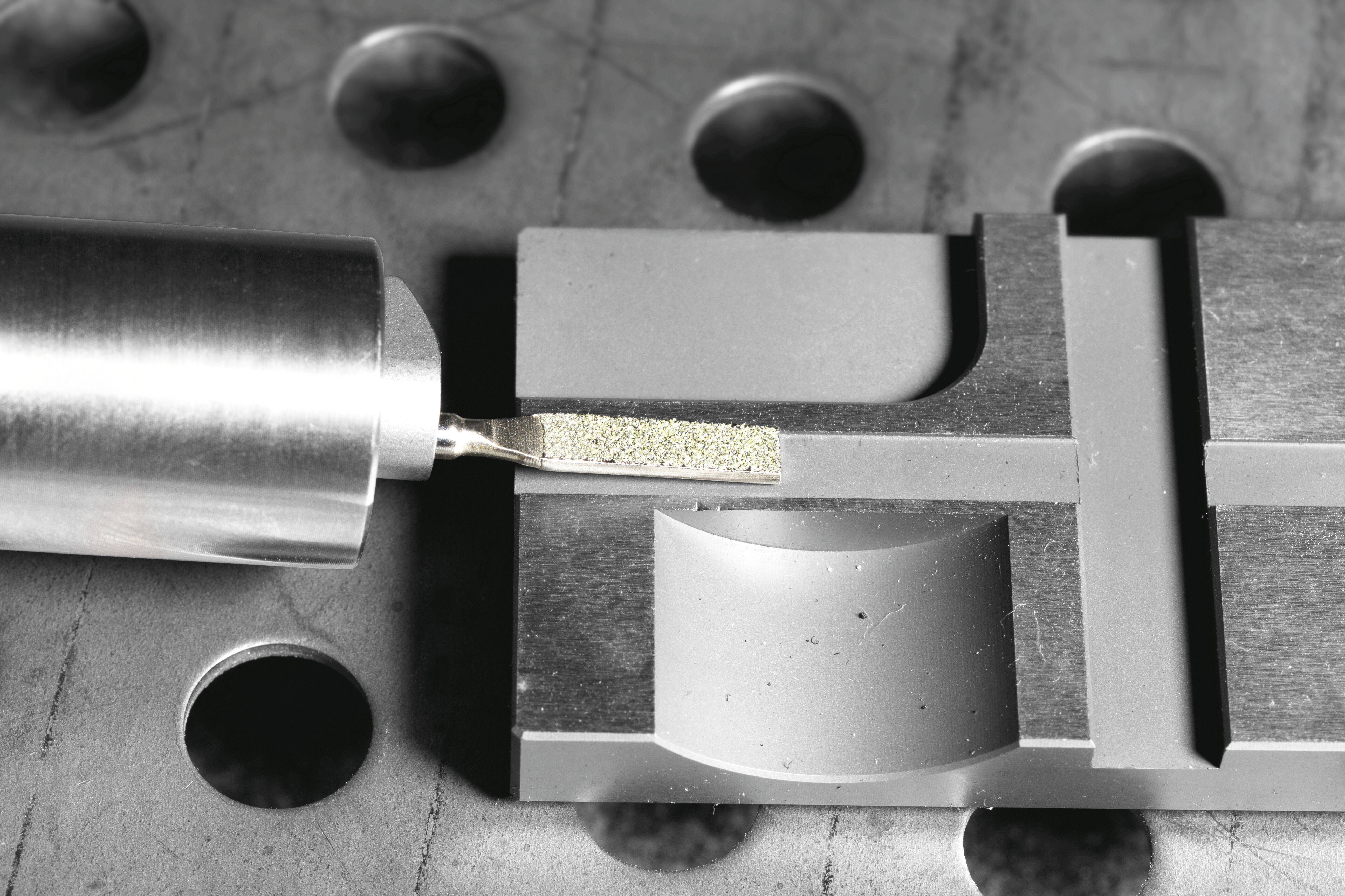 Element mechaniczny na metalowej powierzchni, z narzędziem cylindrycznym umieszczonym obok prostokątnej części, prawdopodobnie wskazujący na regulację lub analizę.