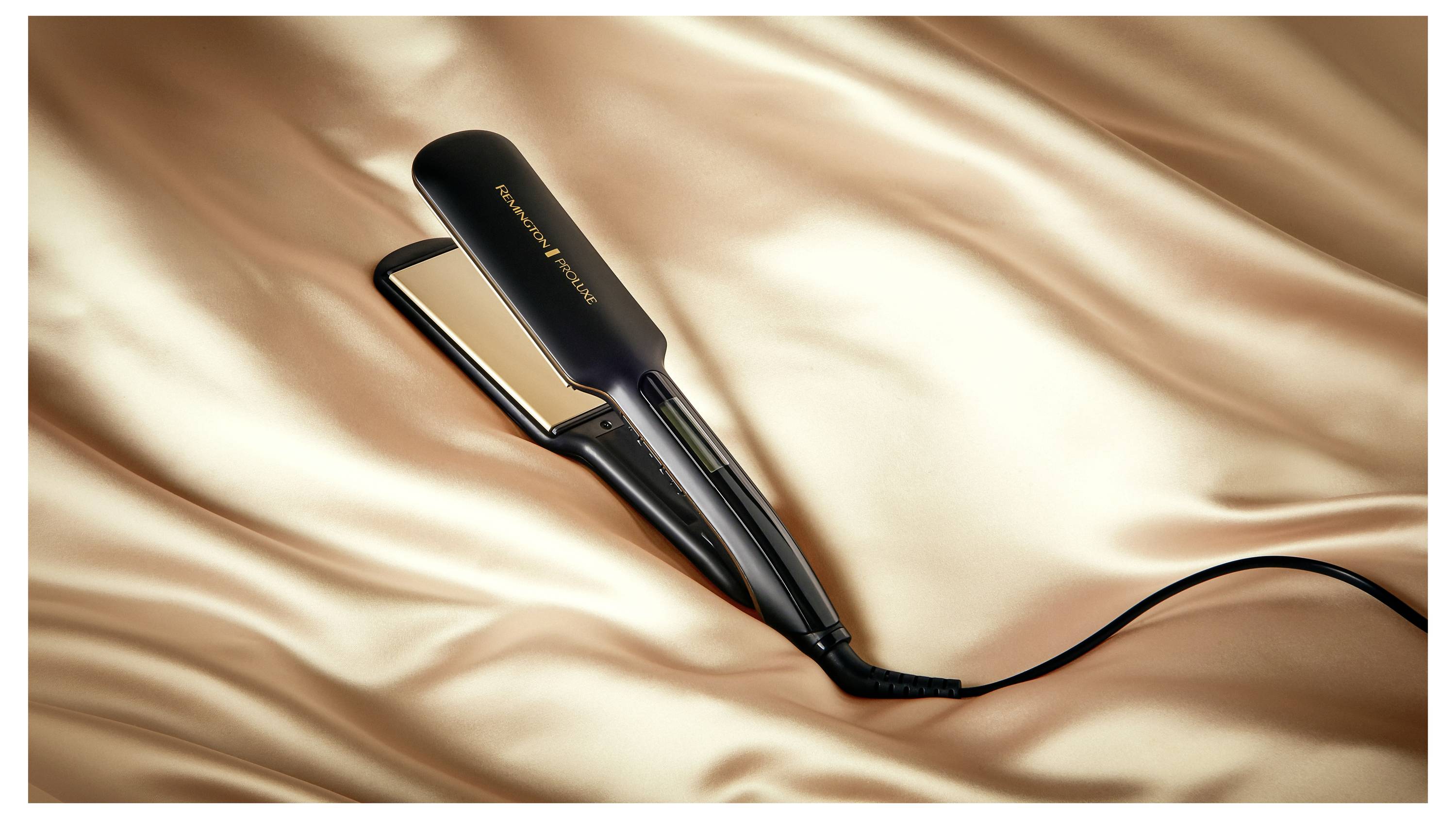 Czarna prostownica do włosów spoczywa na gładkim, jedwabistym tle tkaniny. Nazwa marki jest widoczna na prostownicy.