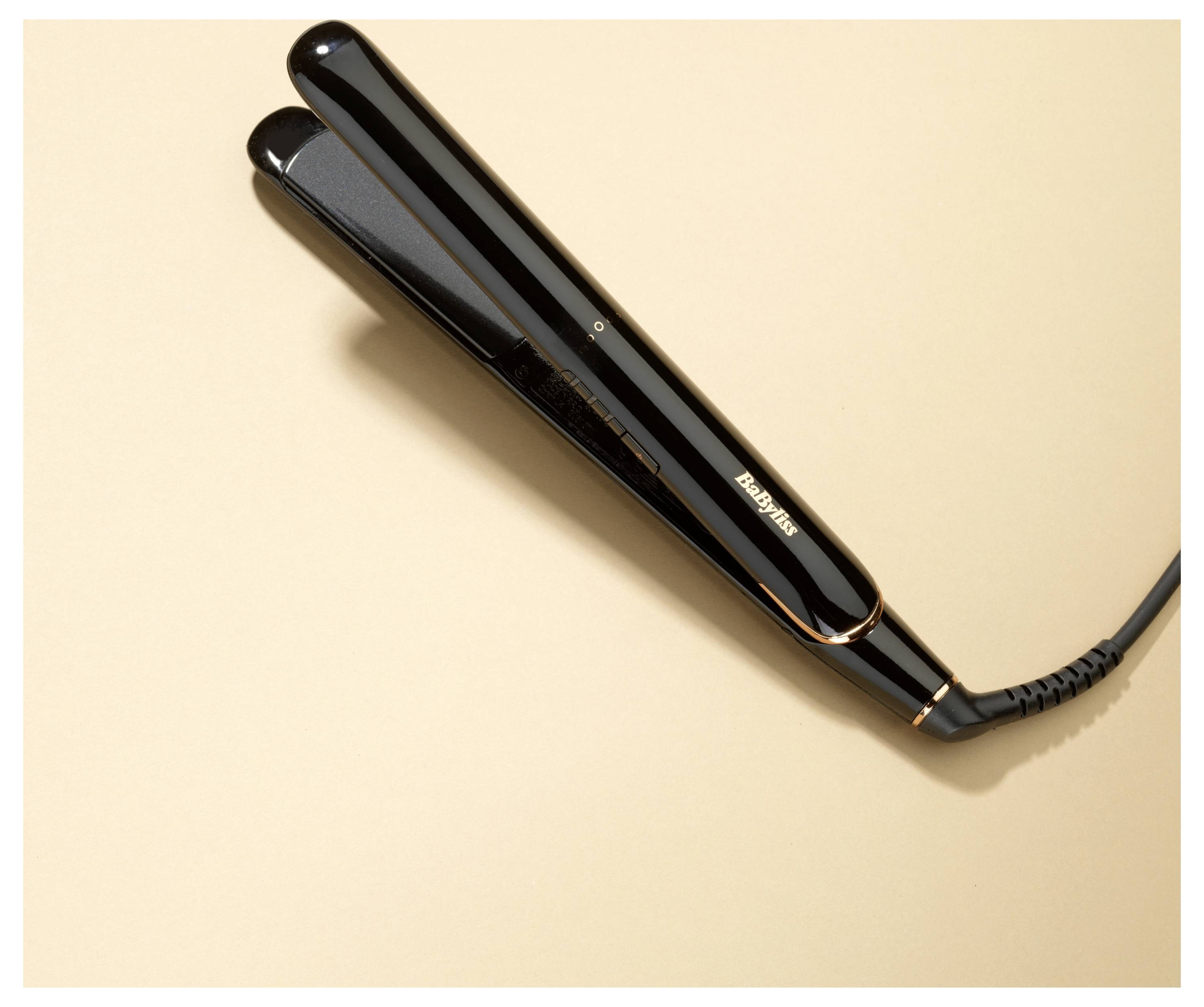 Czarna prostownica do włosów leży na beżowej powierzchni, prezentując swój elegancki design i przewód.