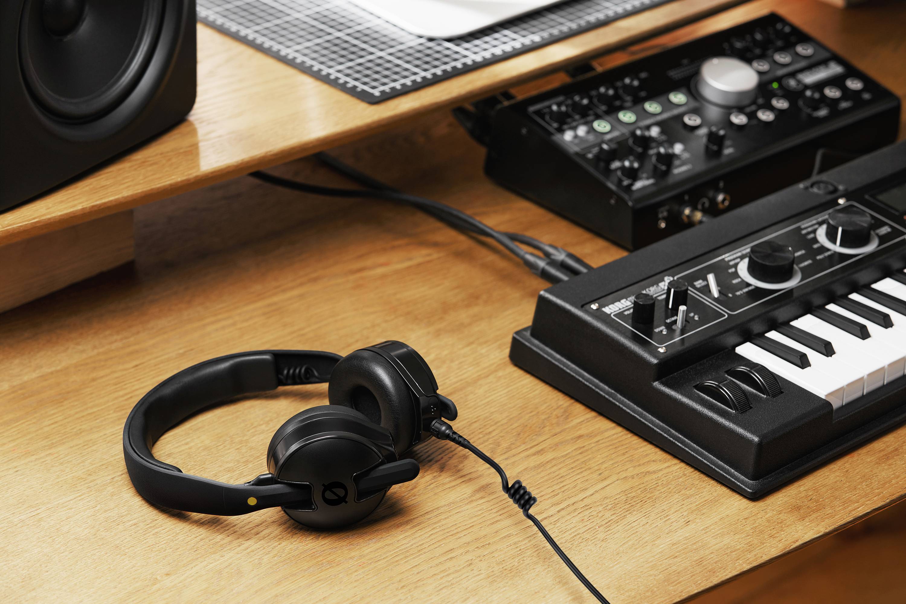 Drewniany biurko stoi z małą klawiaturą, interfejsem audio i słuchawkami, sugerując domowe stanowisko do produkcji muzycznej.