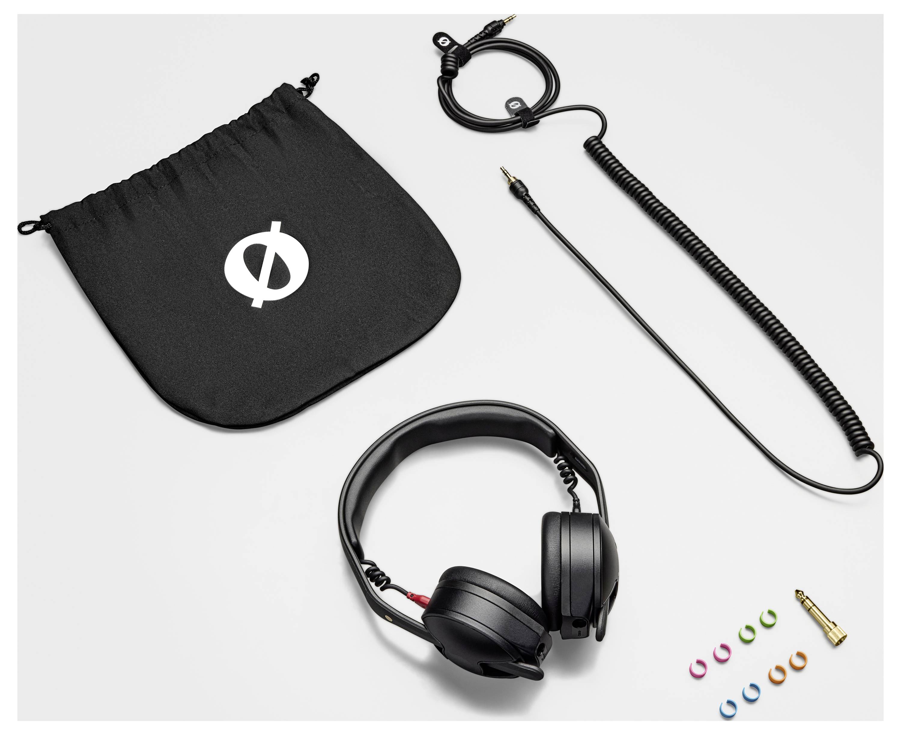 Czarne słuchawki z przewodem spiralnym i prostym, czarny woreczek ze sznurkiem z logo, kolorowymi pierścieniami i adapterem na jasnym tle.
